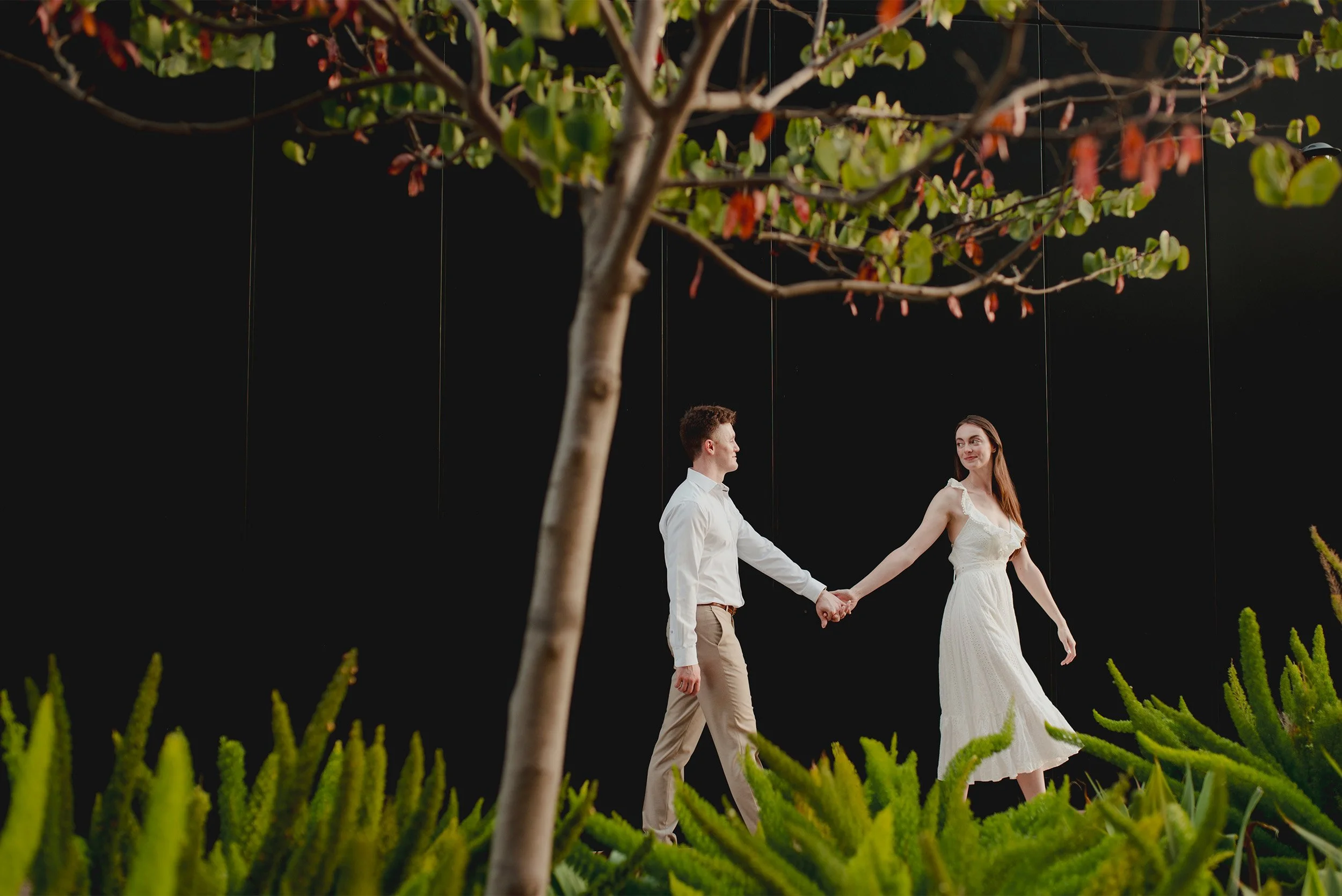Award-winning engagement photographer in Orange County captures couple walking hand in hand against a dramatic dark backdrop