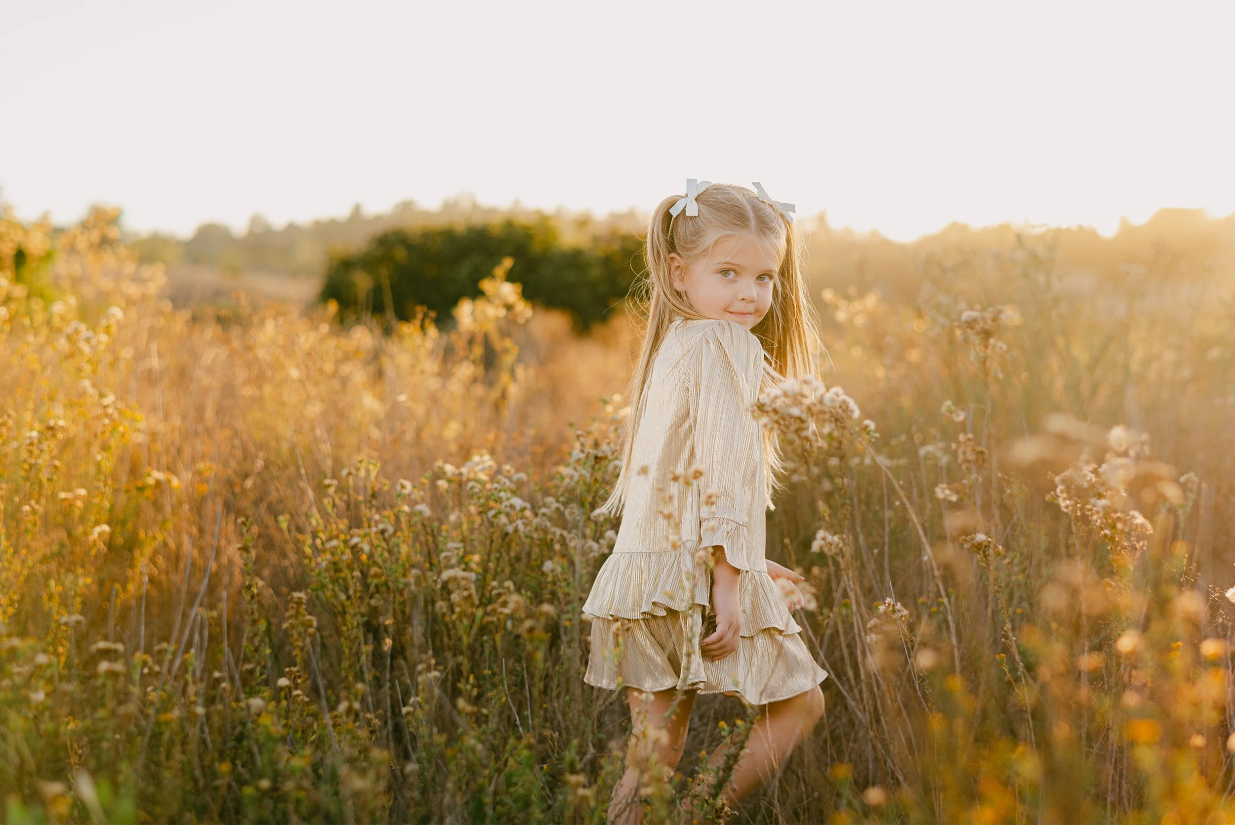 Orange County family photographer captures girl in golden dress looking back in autumn field