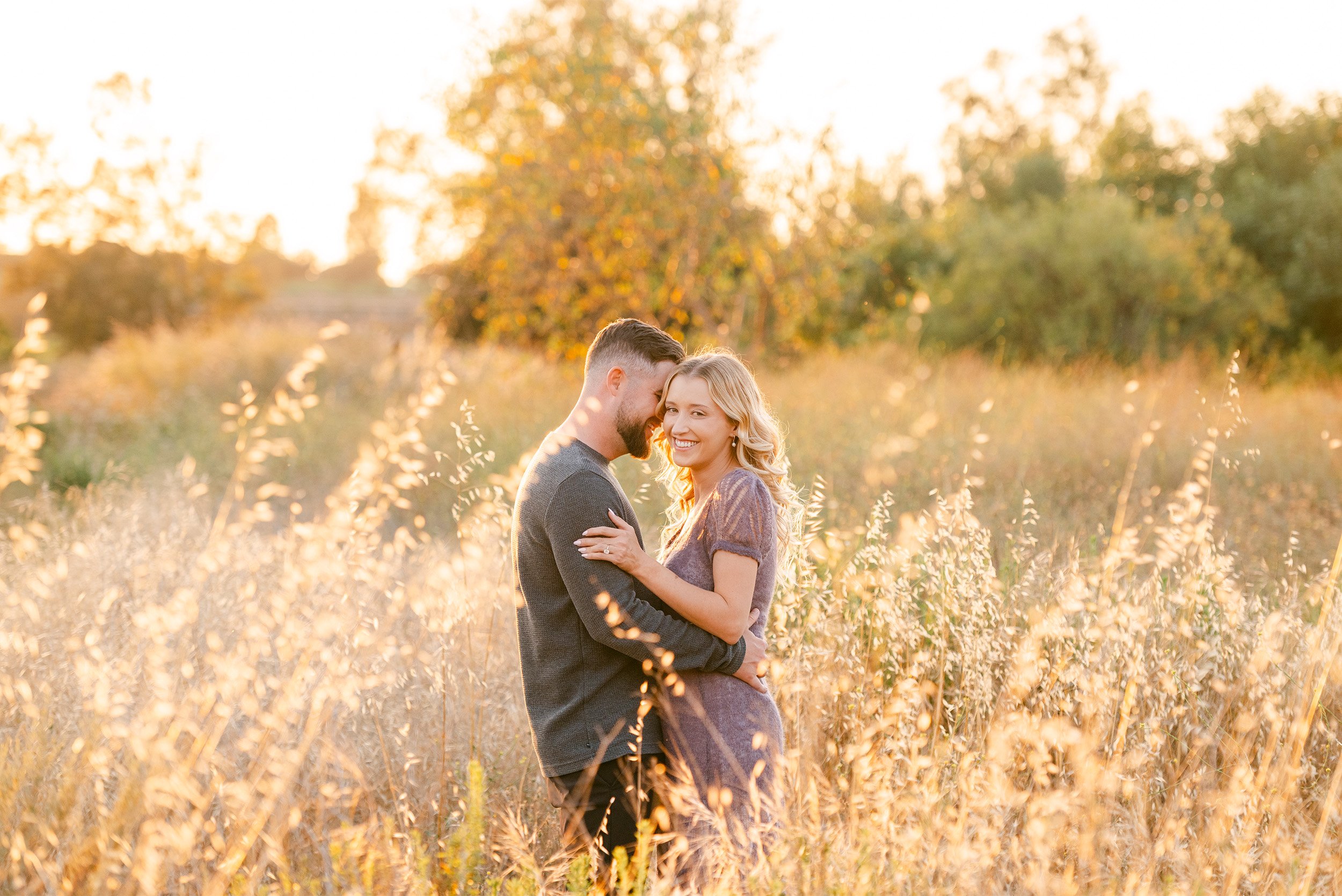 Orange County engagement photographer captures couple embracing in golden field at sunset