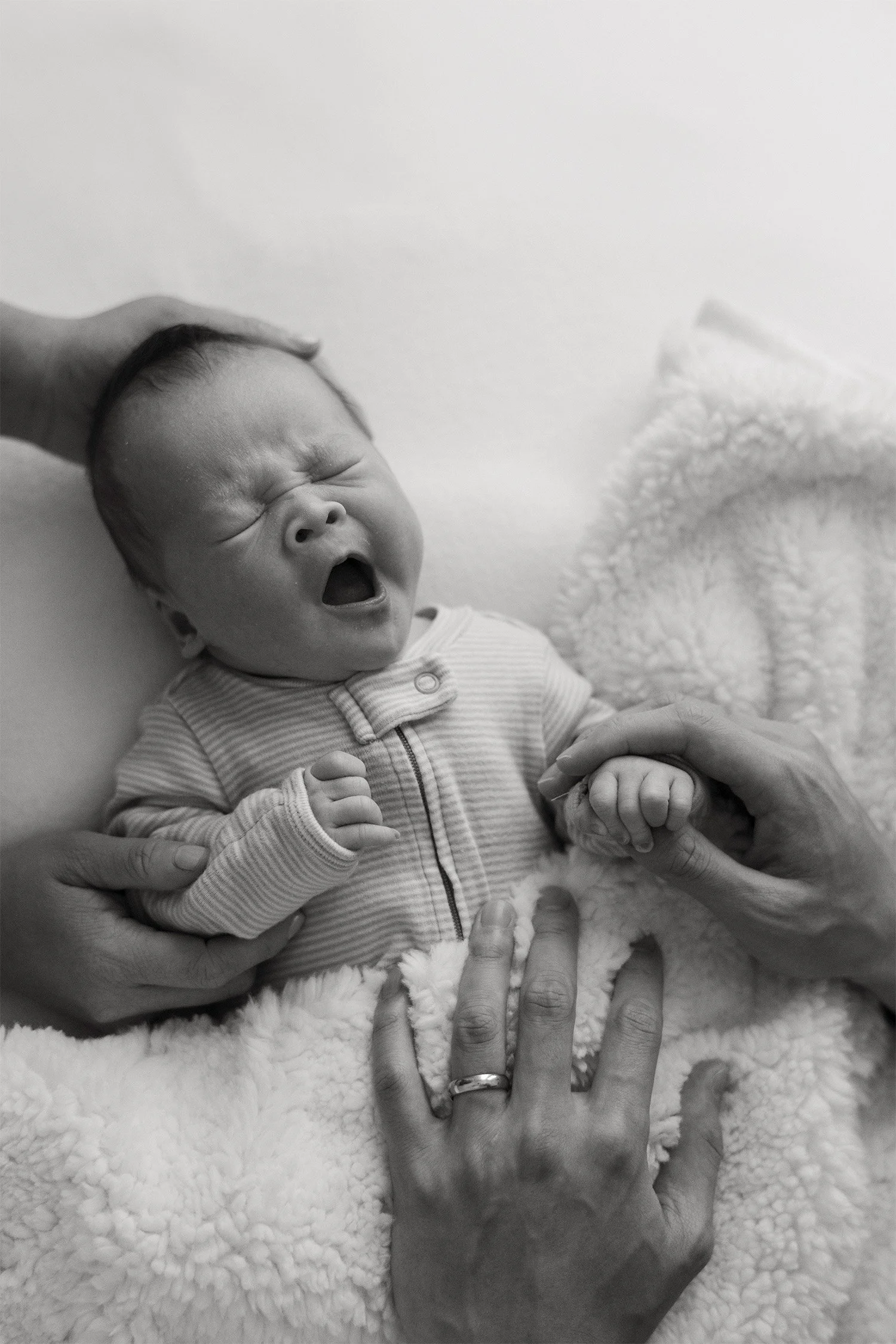 Black and white photo of yawning newborn held by parents' hands, highly recommended baby photographer Orange County