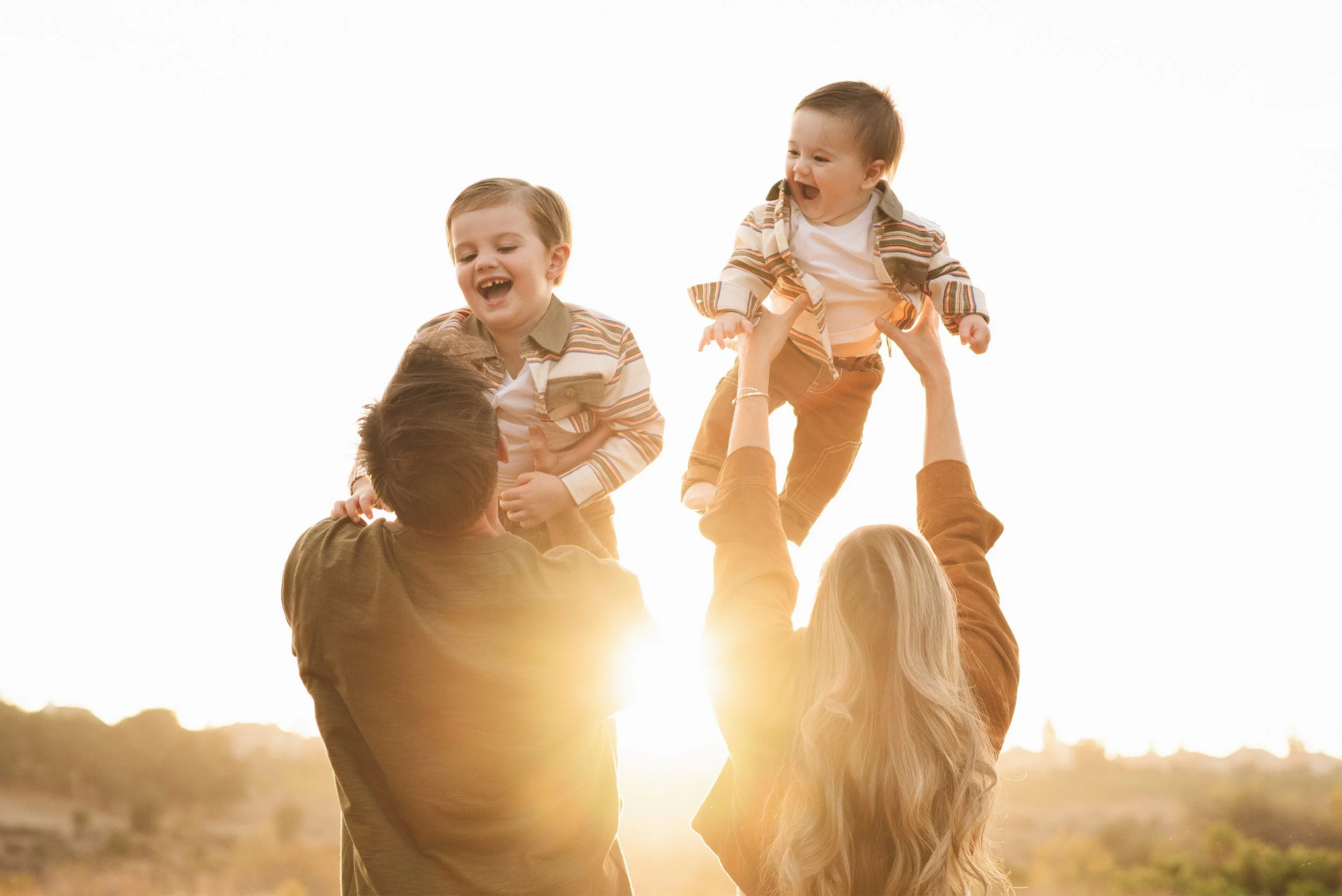 Orange County family photographer captures parents lifting laughing toddlers at sunset in Irvine Park