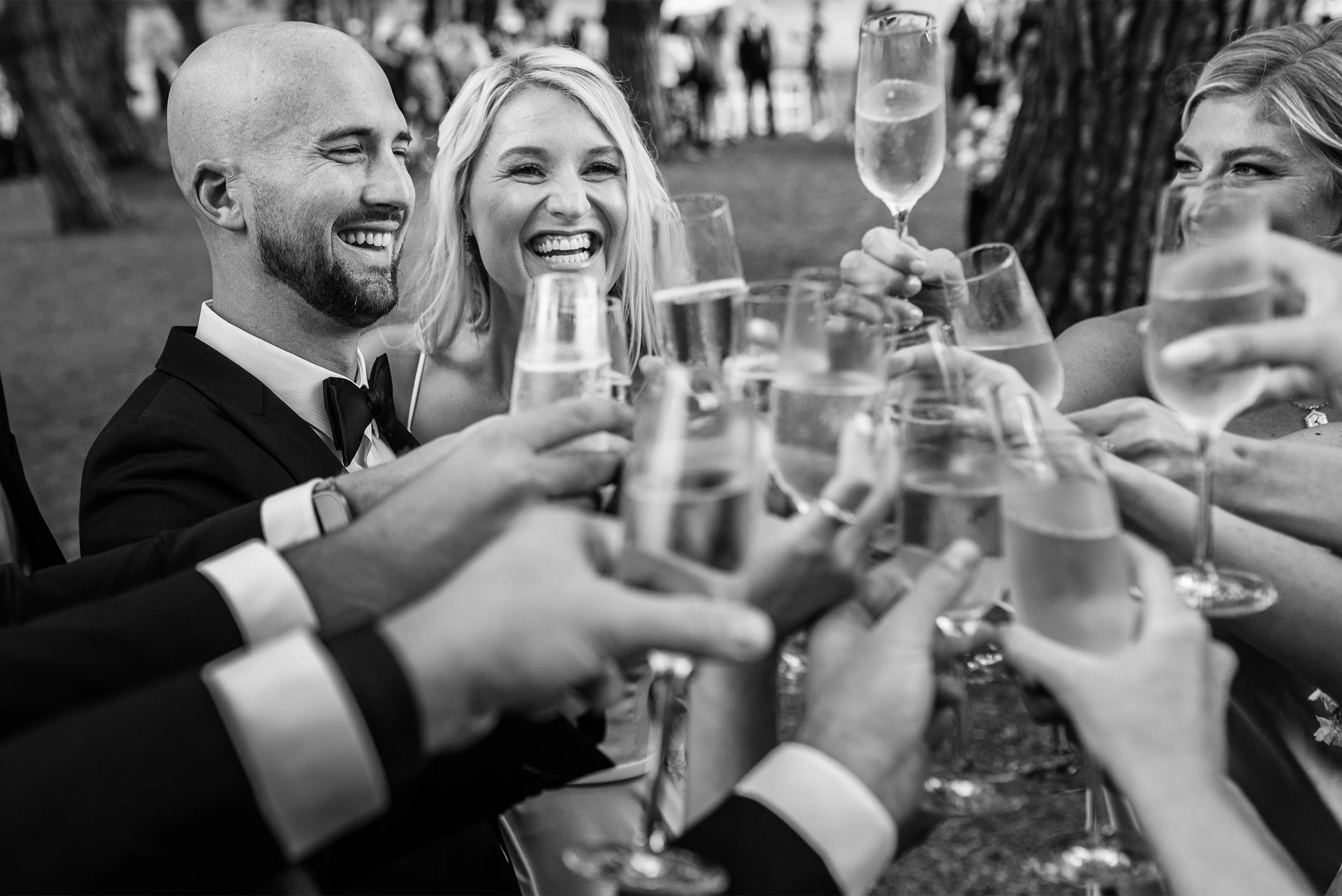 Orange County wedding photographer captures joyful champagne toast with bride and groom laughing among guests at The Ranch at Laguna Beach, black and white