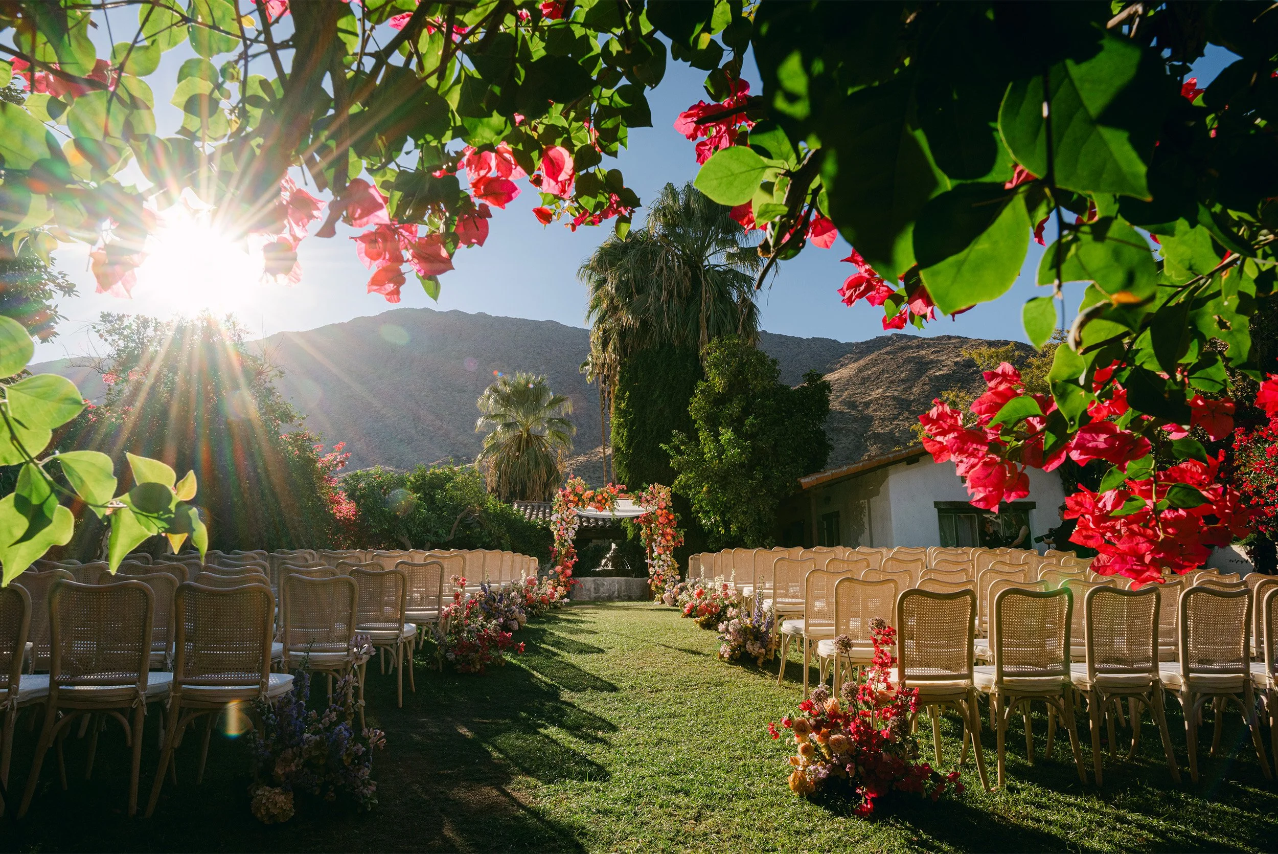 Empty wedding ceremony chairs framed by bougainvillea flowers with mountain views, desert garden wedding venue Casa Cody Palm Springs