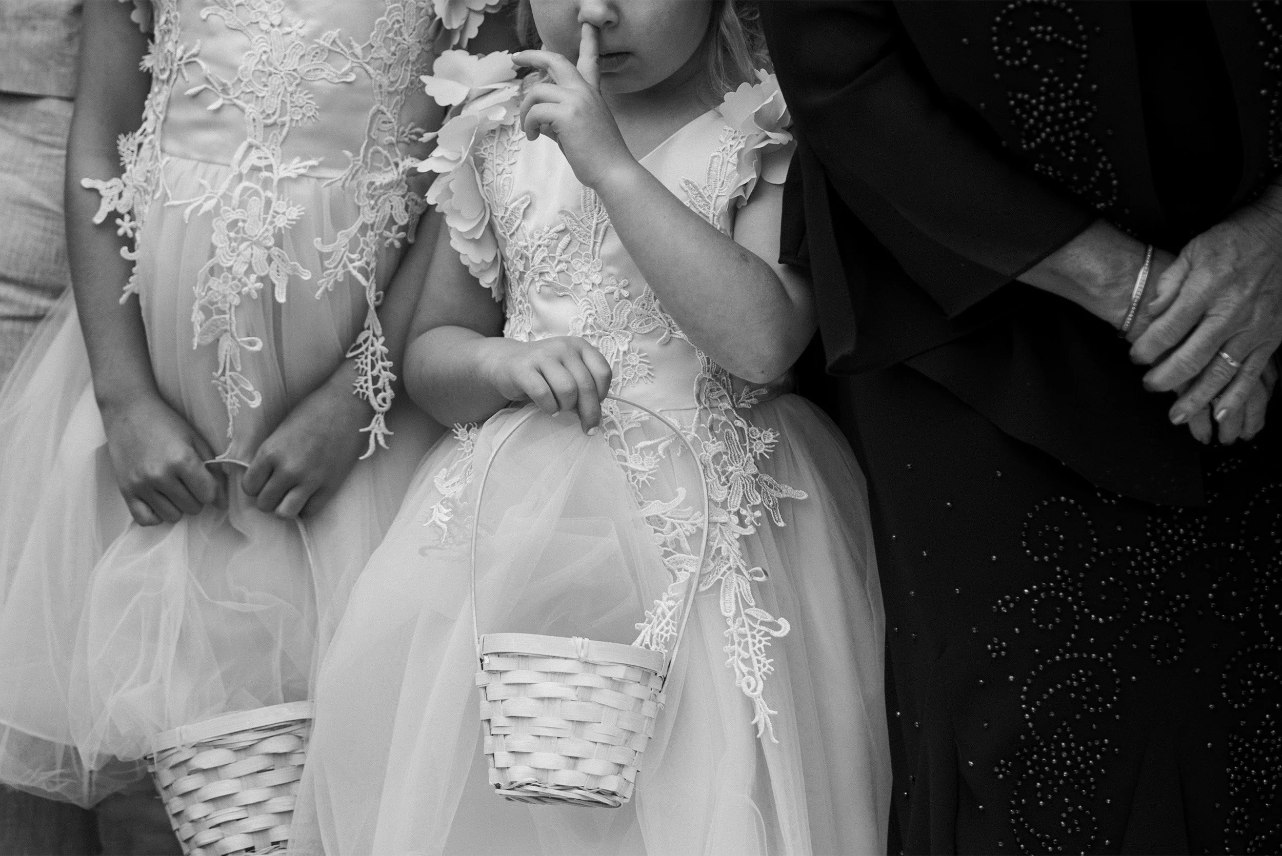 Flower girl holding basket with finger in her nose, black and white wedding detail photo