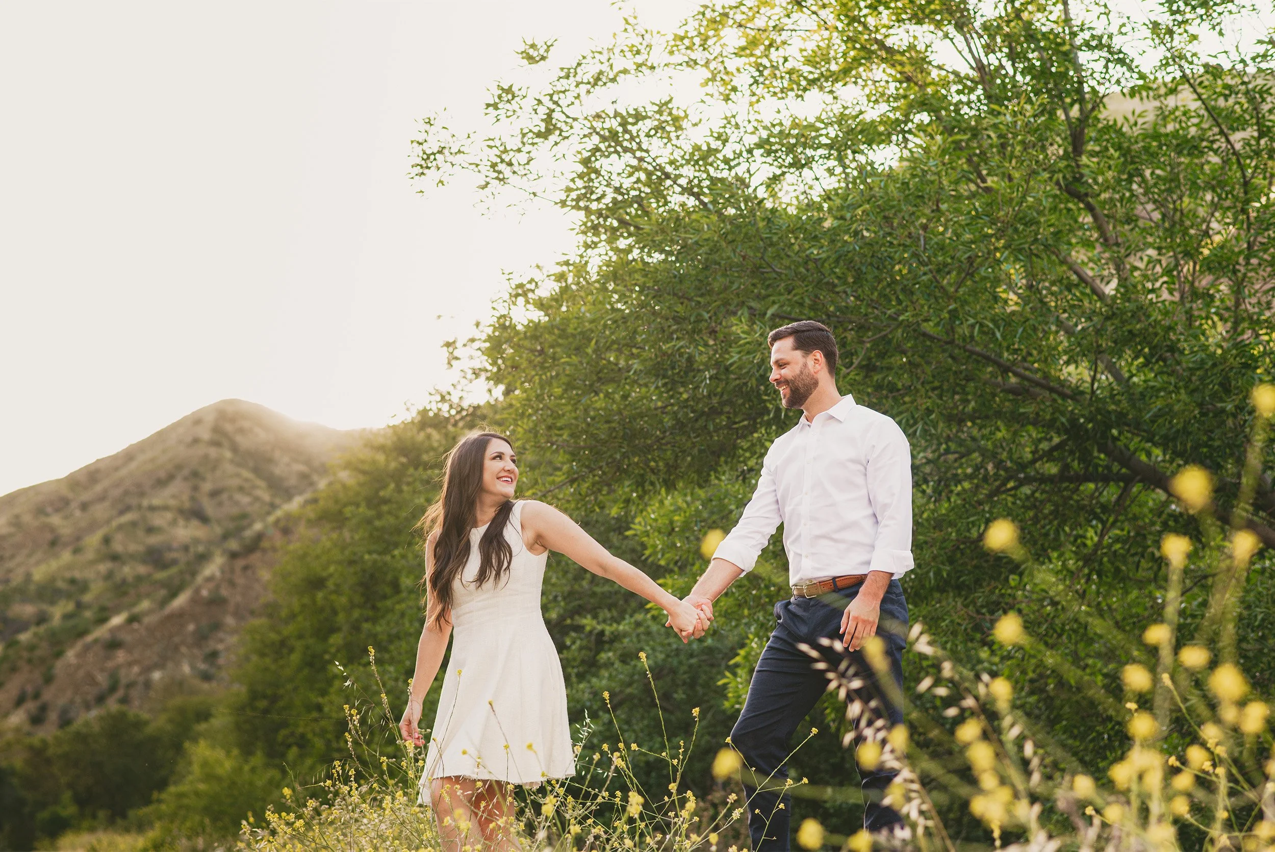 Couple walking hand in hand through green hillside meadow, award-winning engagement photographer in Orange County