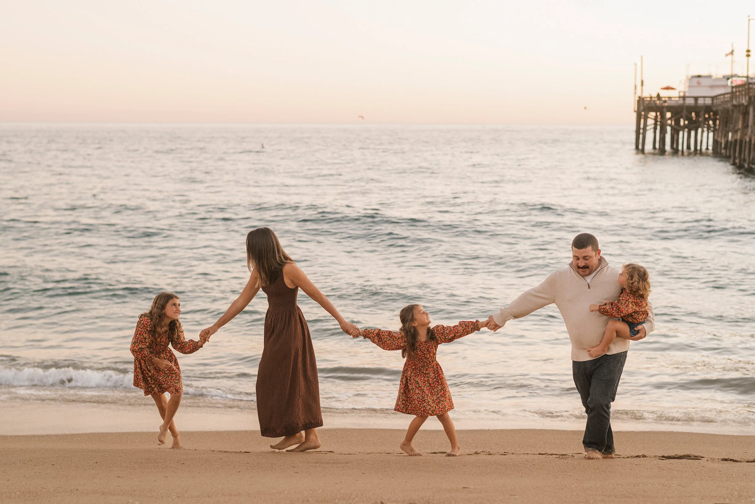 Orange County family photographer captures family walking hand-in-hand on beach at sunset