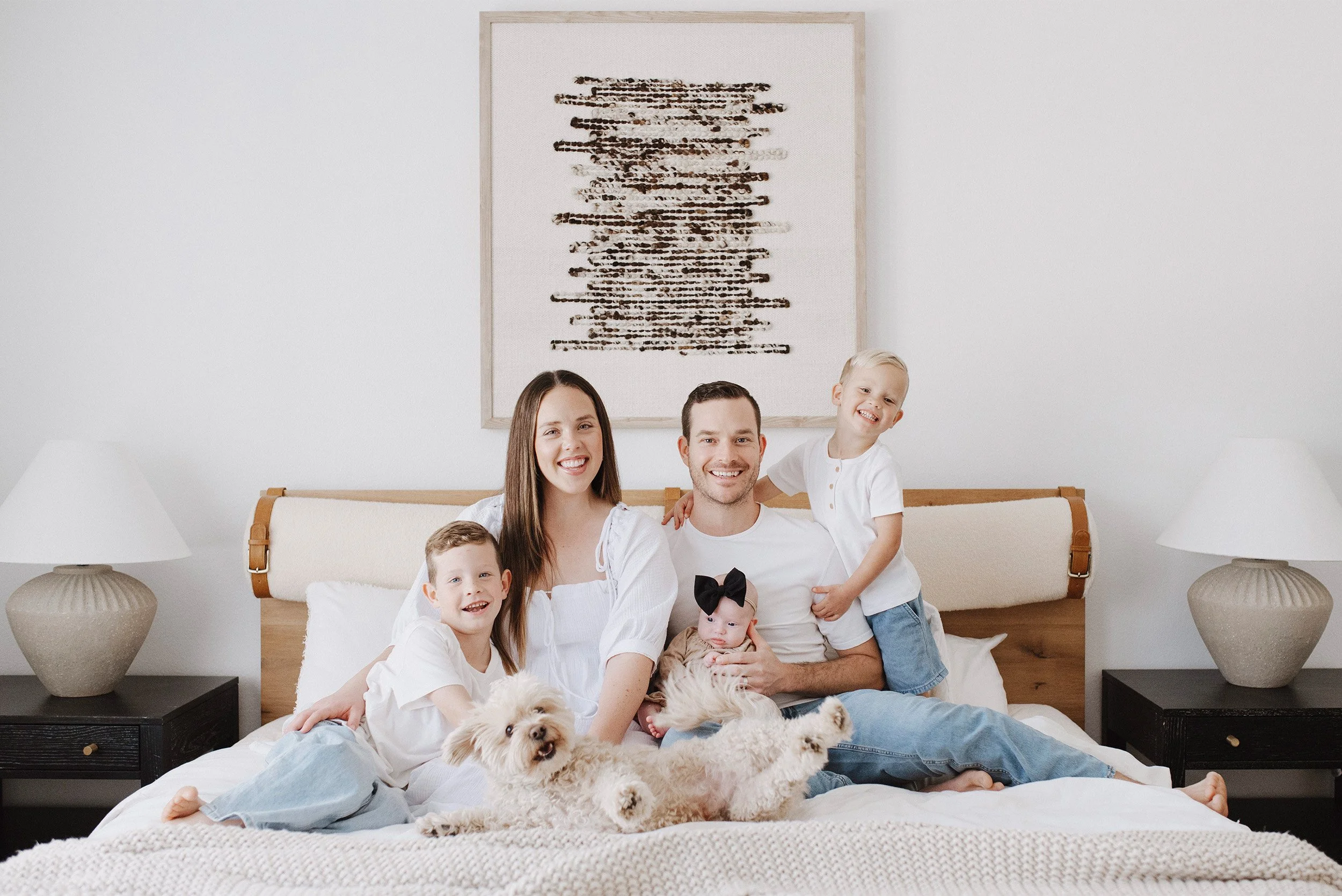 Family of five smiling with the sons, newborn, and dog on their bed, Orange County baby pet-friendly photographer