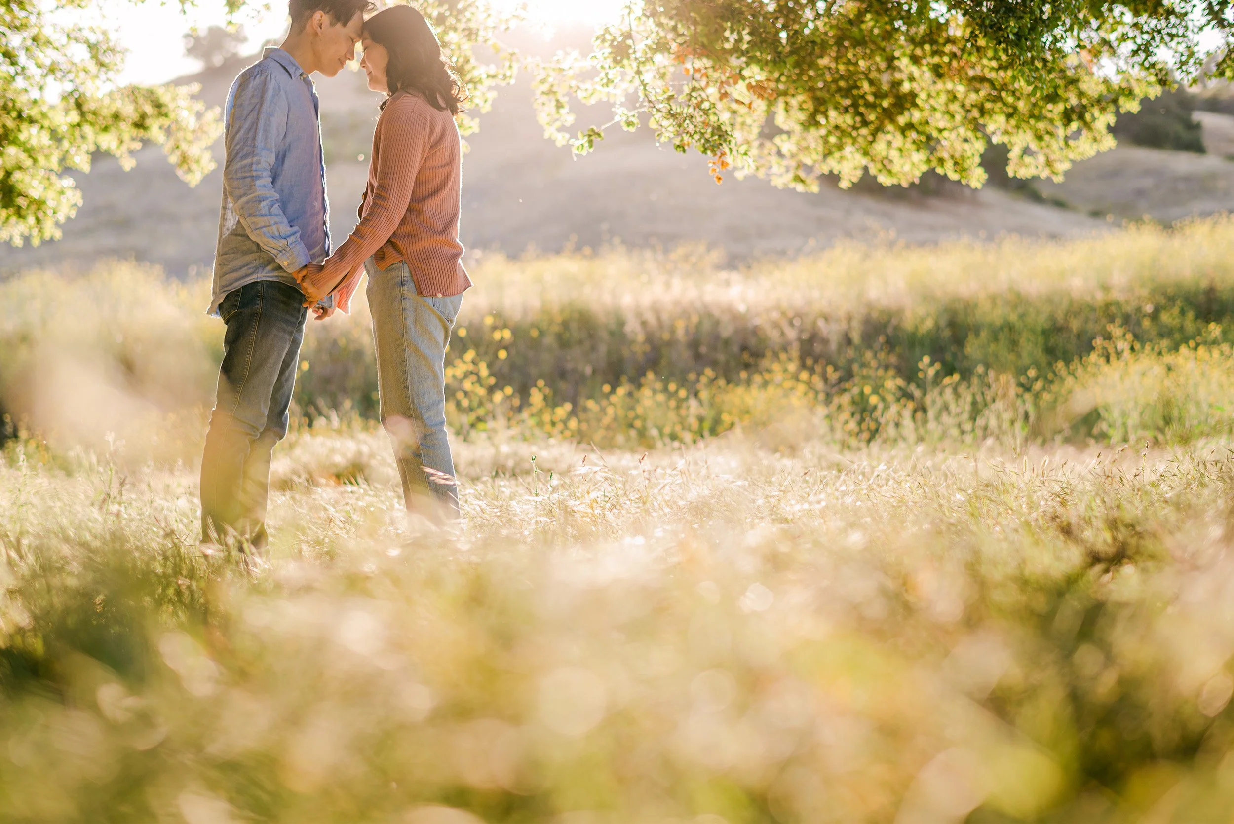 Couple sharing an intimate moment under oak tree in golden light, award-winning engagement photographer in Orange County