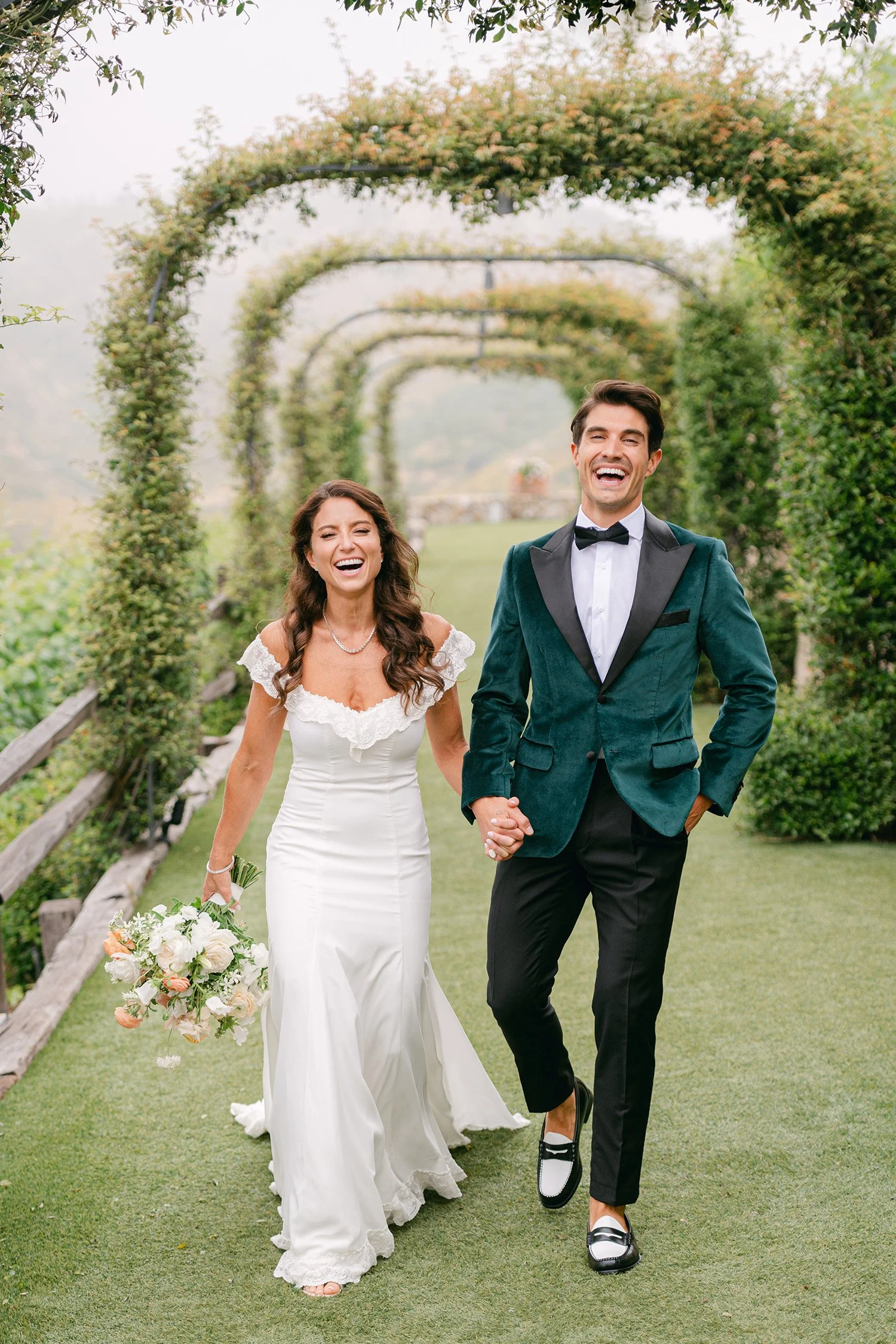 Award-winning wedding photographer in Orange County captures joyful bride and groom laughing beneath vine-covered garden arbor walkway at Cielo Farms in Malibu wine country