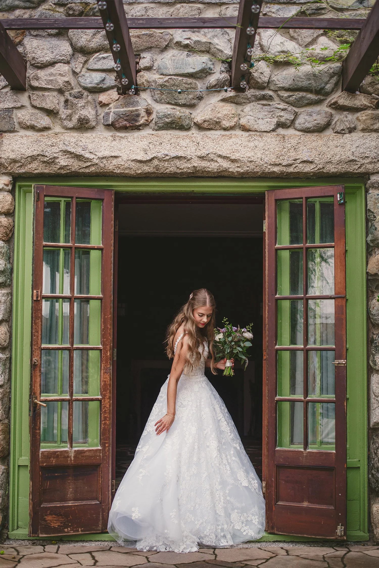 Destination wedding photographer captures bride in lace ball gown stepping through rustic stone doorway with green trim in Boston