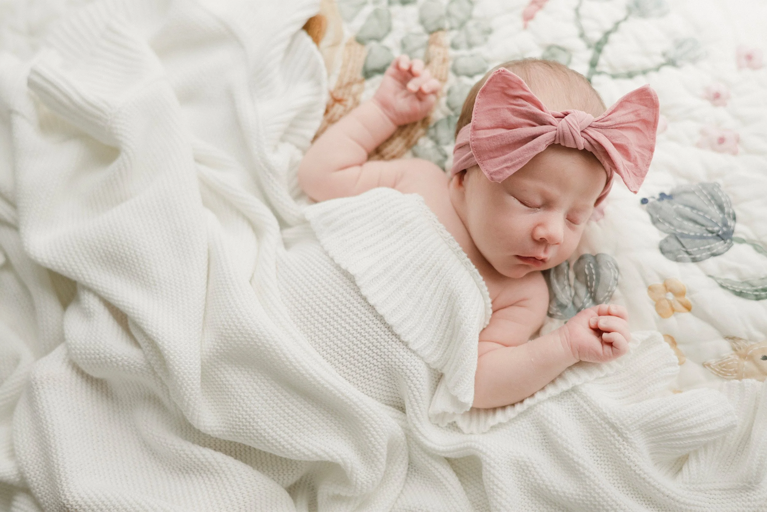 Sleeping newborn in pink bow headband wrapped in white knit blanket, award-winning baby photographer in Orange County