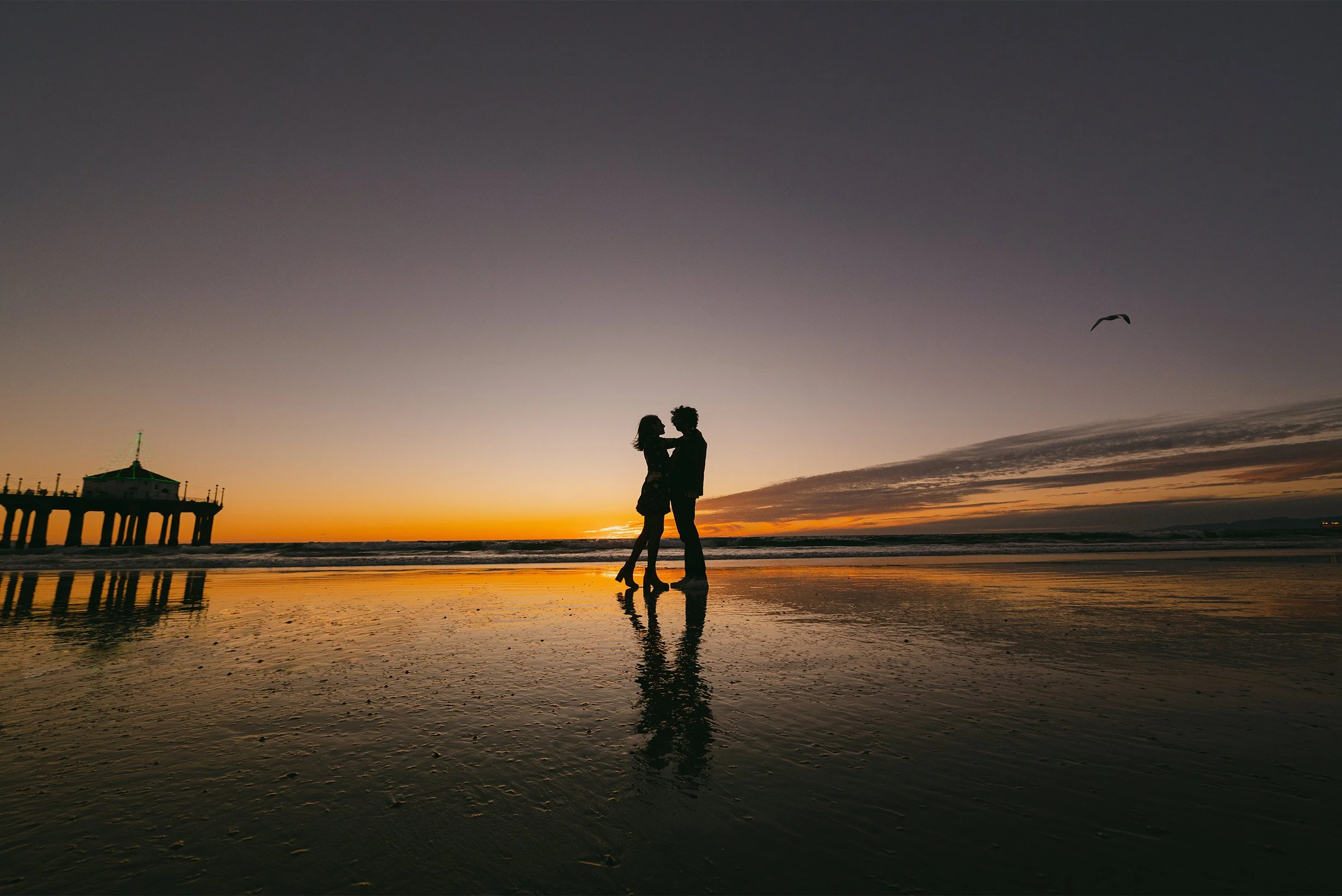 Orange County engagement photographer captures silhouetted couple embracing near the pier in Manhattan Beach at sunset