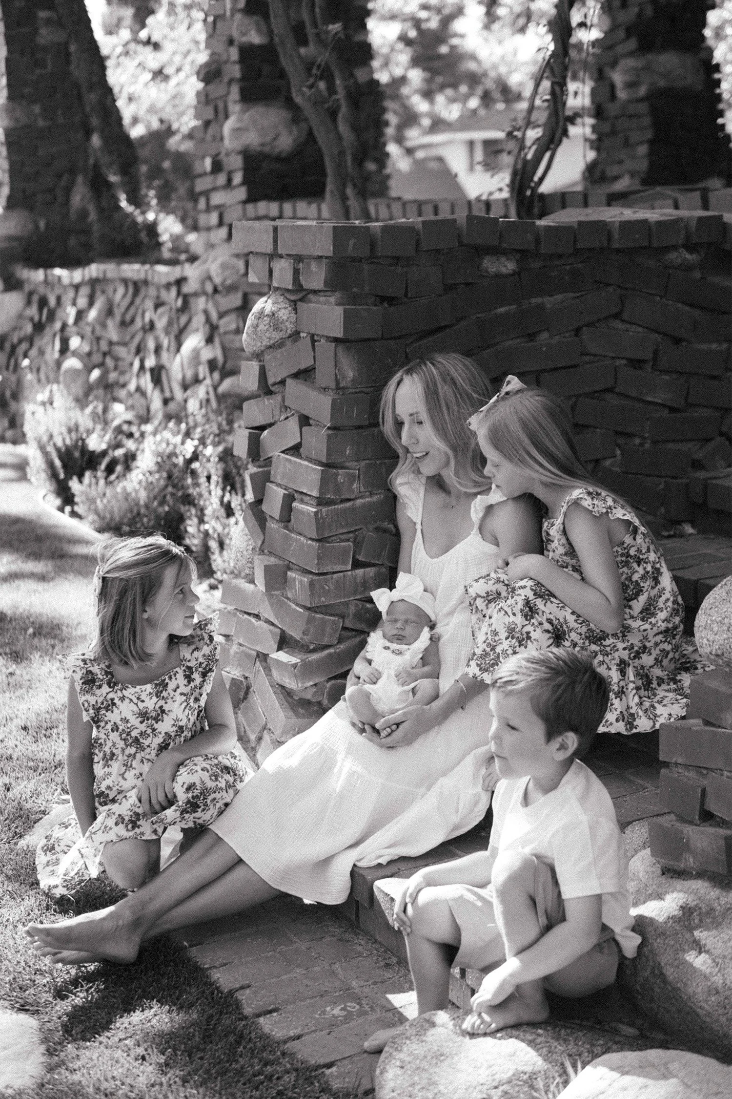 Family photography session featuring mother and four children seated together on a brick garden wall in Orange County