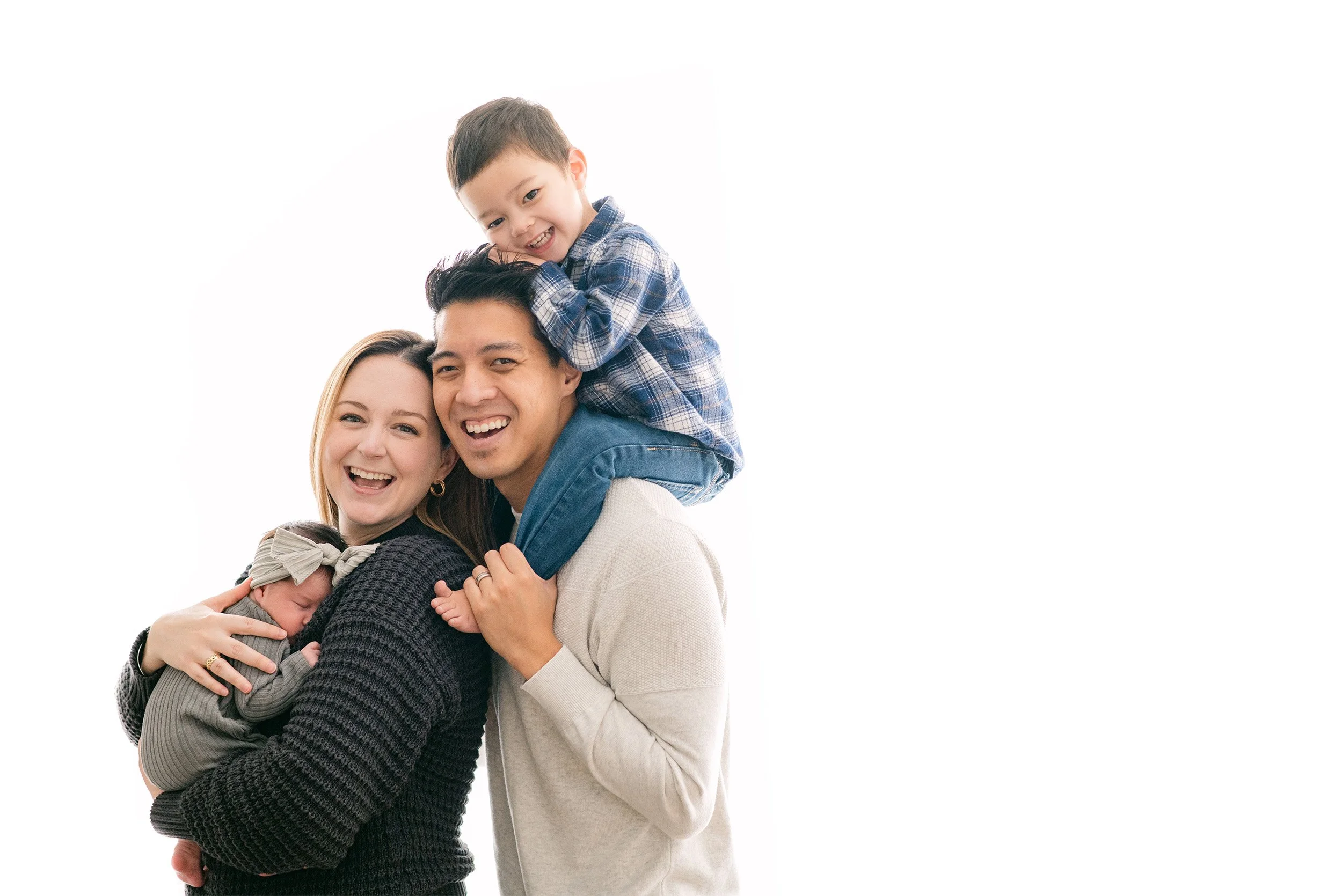 Laughing family of four with newborn and toddler on white backdrop, award-winning newborn photographer in Orange County