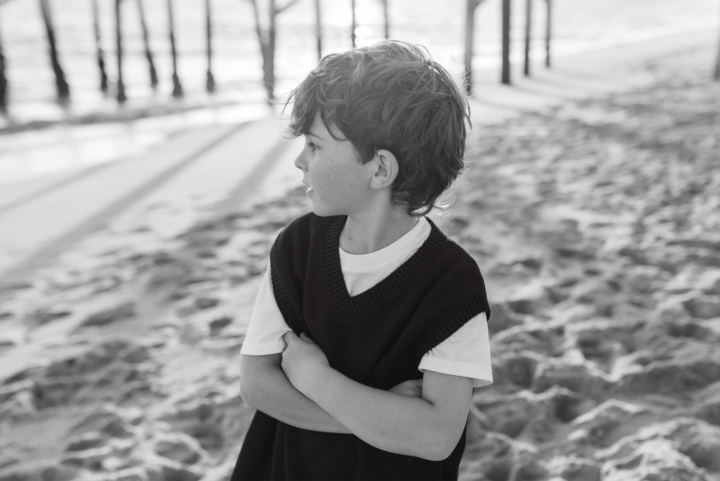 Black and white beach portrait of young boy in sweater vest looking out to sea, Orange County family photographer
