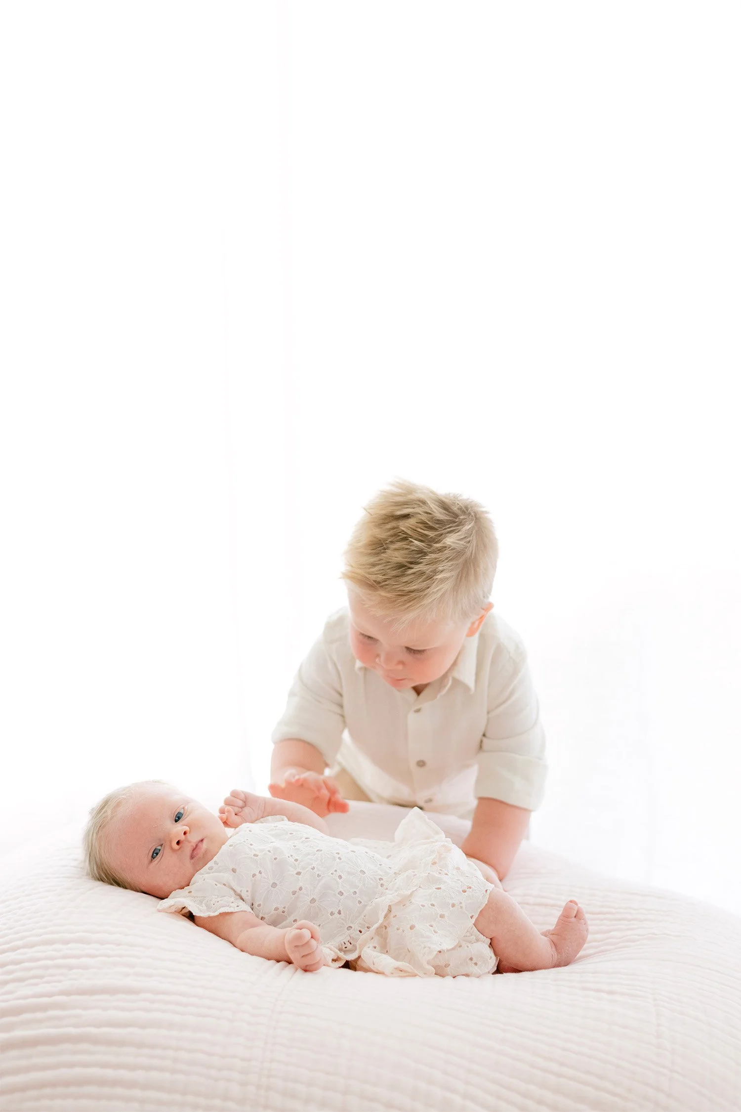 Big brother reaching to touch newborn sister lying on bed, Orange County newborn photographer