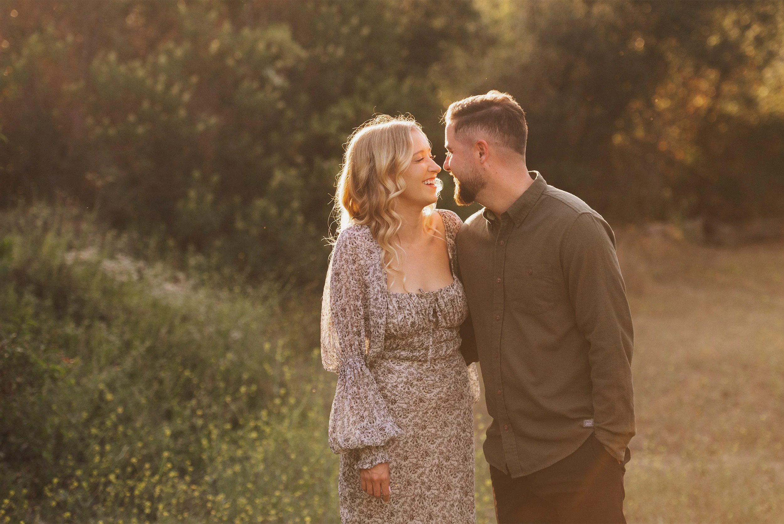 Award-winning engagement photographer in Orange County captures couple laughing nose to nose in a sunlit field