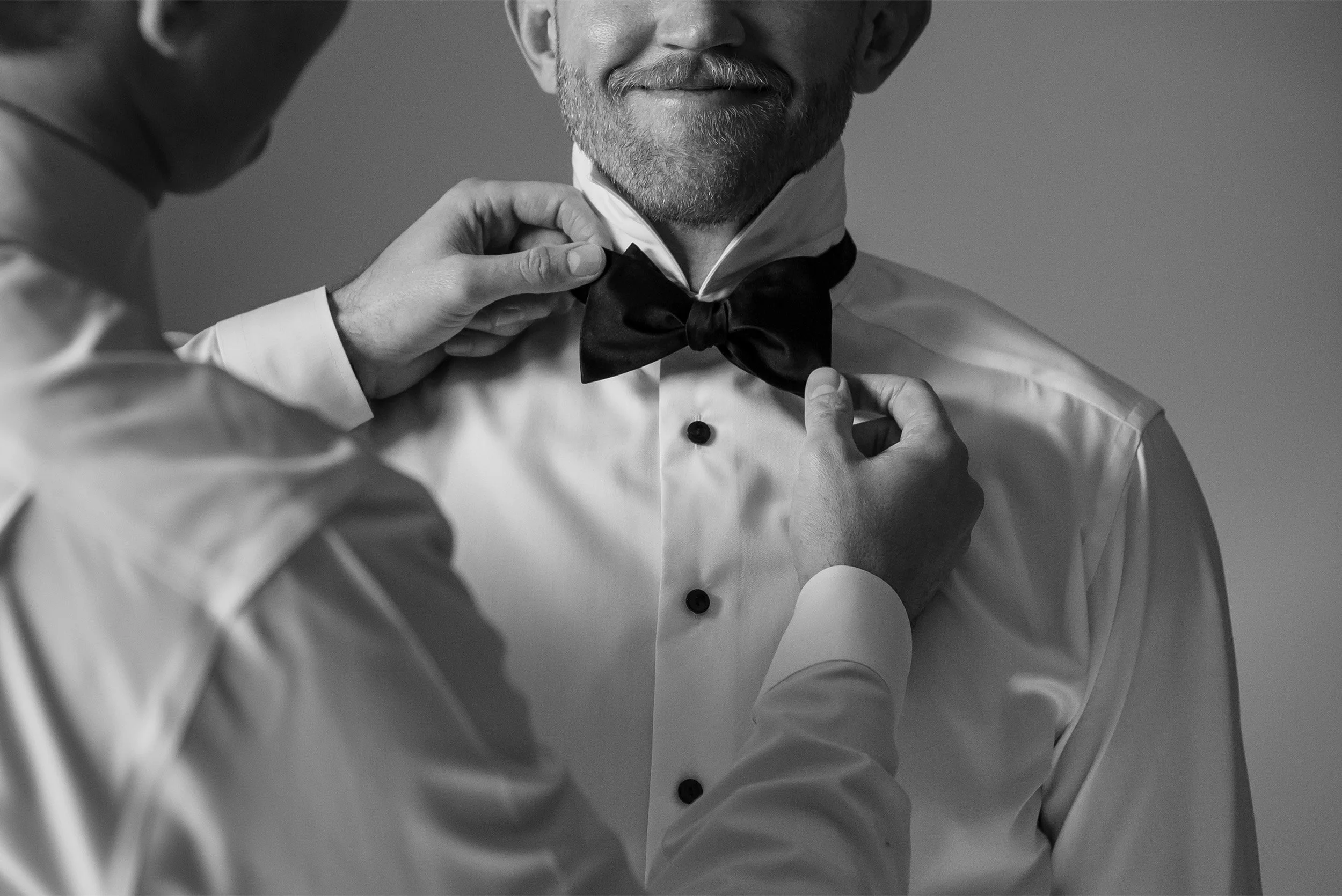 Award-winning Laguna Beach wedding photographer captures detailed close-up of groom having his bow tie adjusted at The Ranch at Laguna Beach, black and white