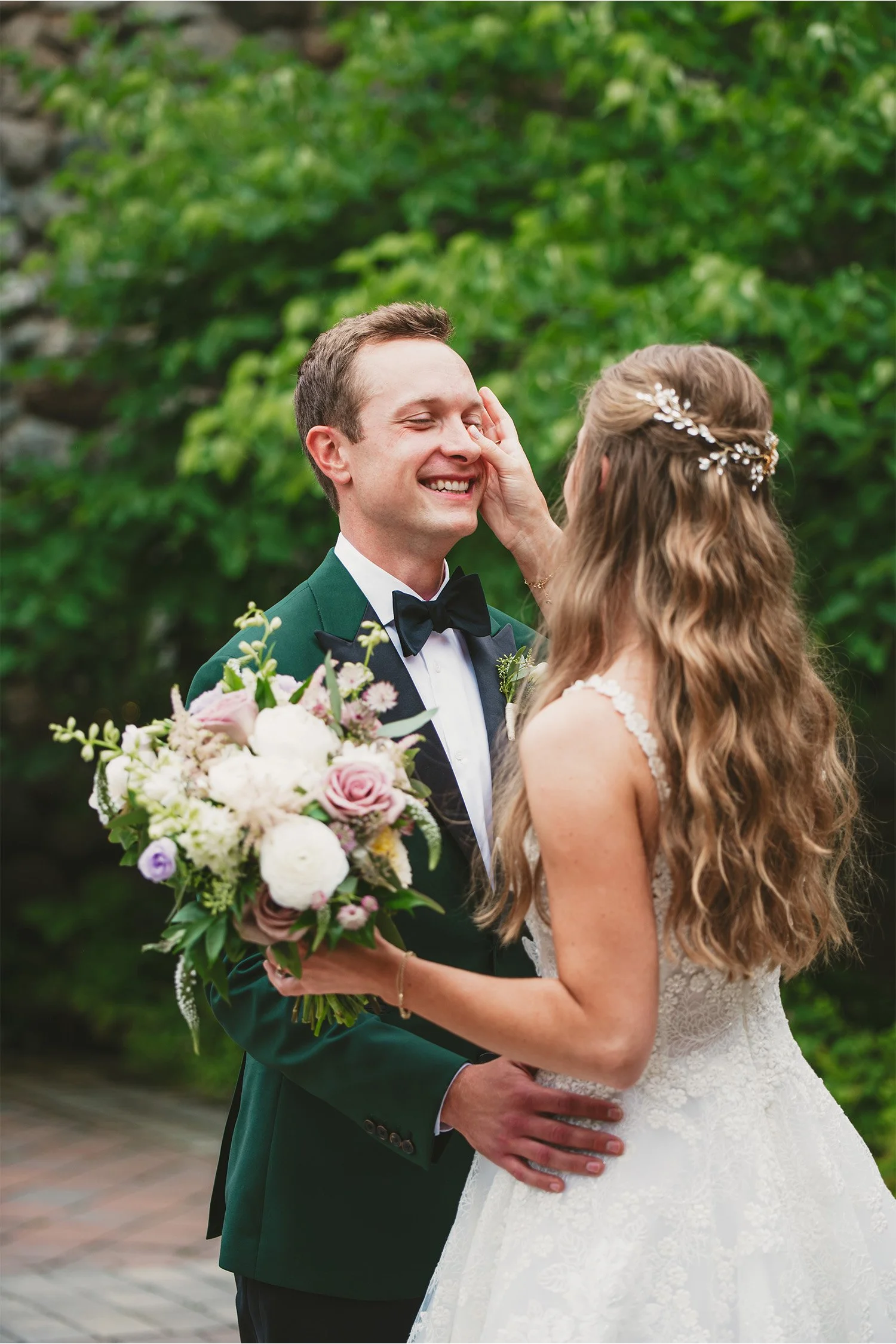 Bride touching groom's face tenderly while she holds bouquet, green tuxedo wedding portrait
