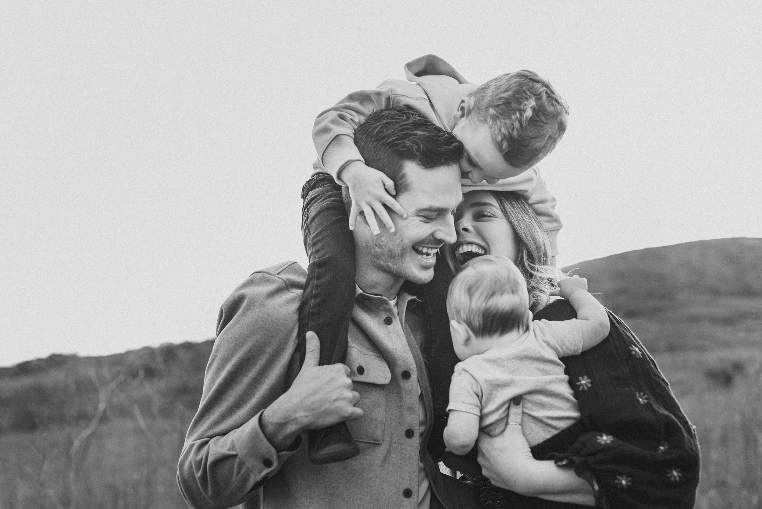 Orange County family photographer captures candid black and white portrait of parents laughing with three children on hillside