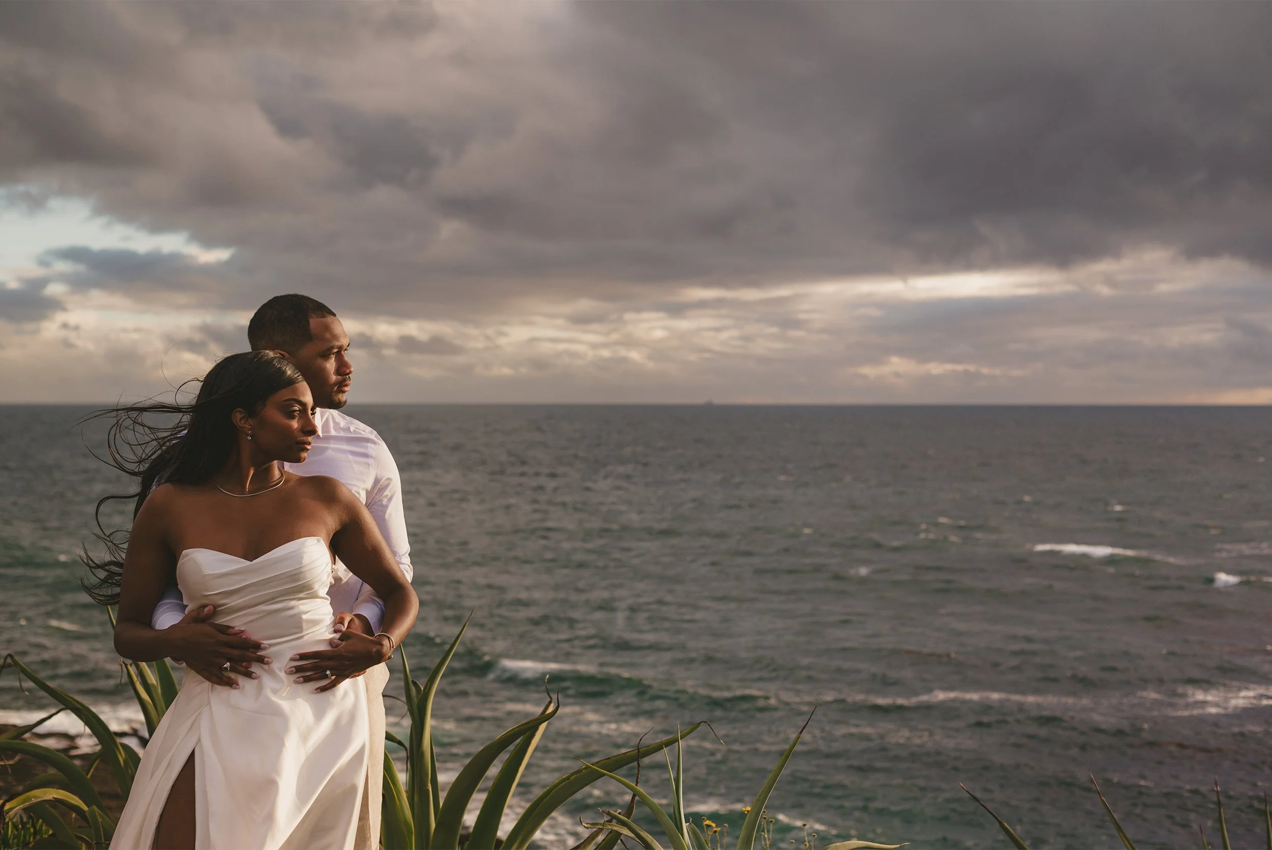 Bride and groom embracing on a coastal cliff overlooking the ocean at sunset at The Montage Laguna Beach, Orange County wedding photography