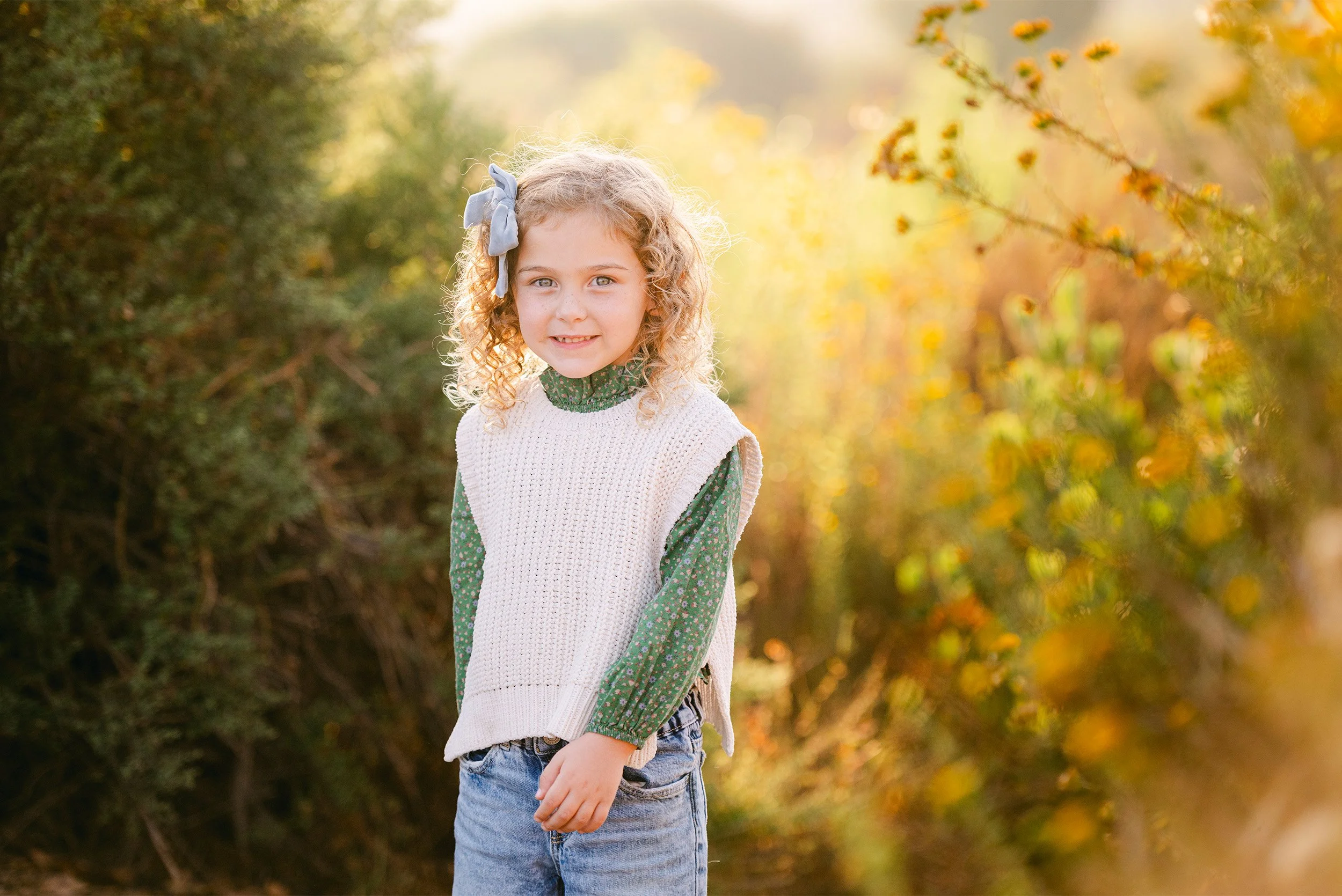 Orange County family photographer captures curly-haired girl smiling in golden hour field