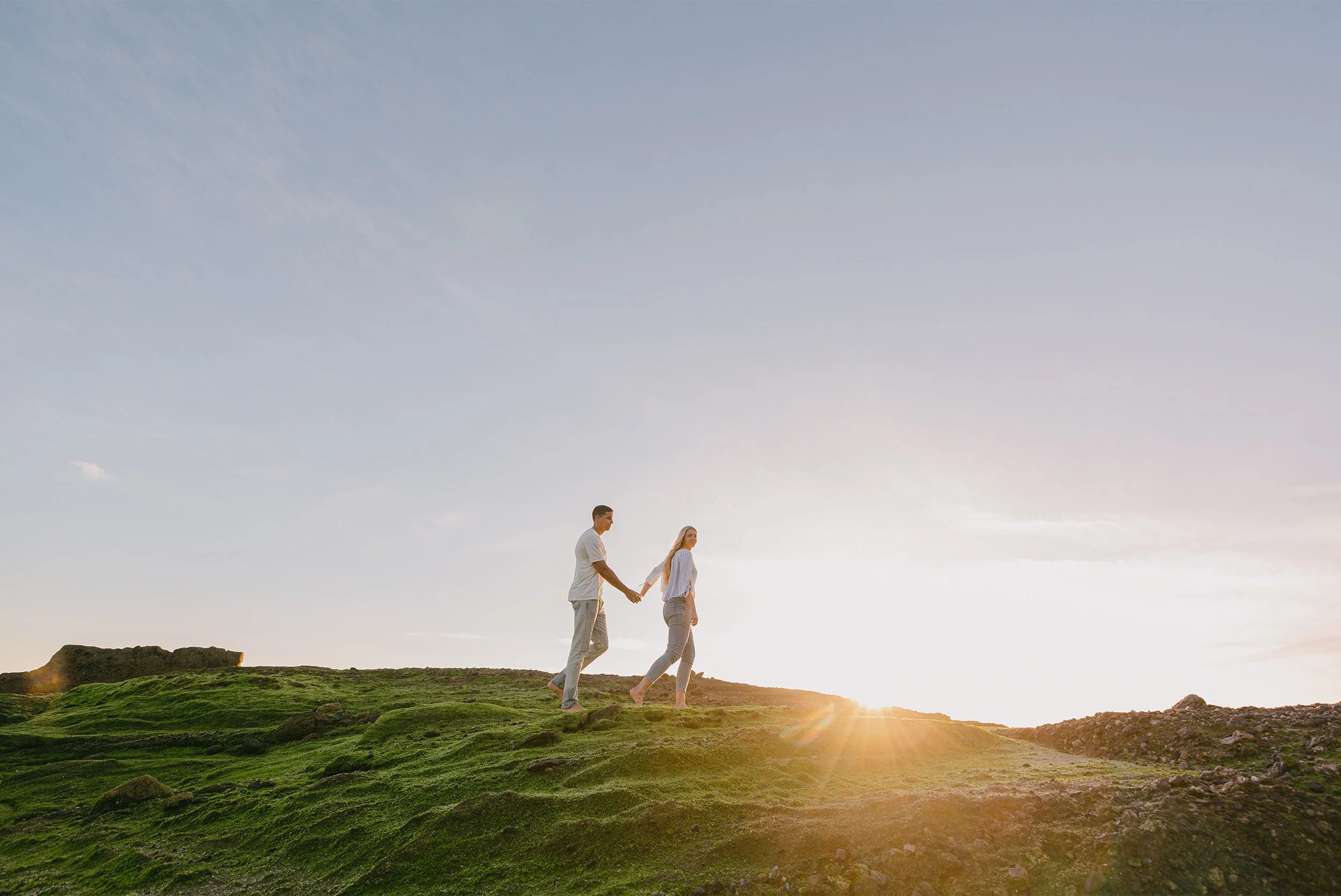 Orange County engagement photographer captures couple holding hands atop a  Laguna Beach coastal hill at sunset