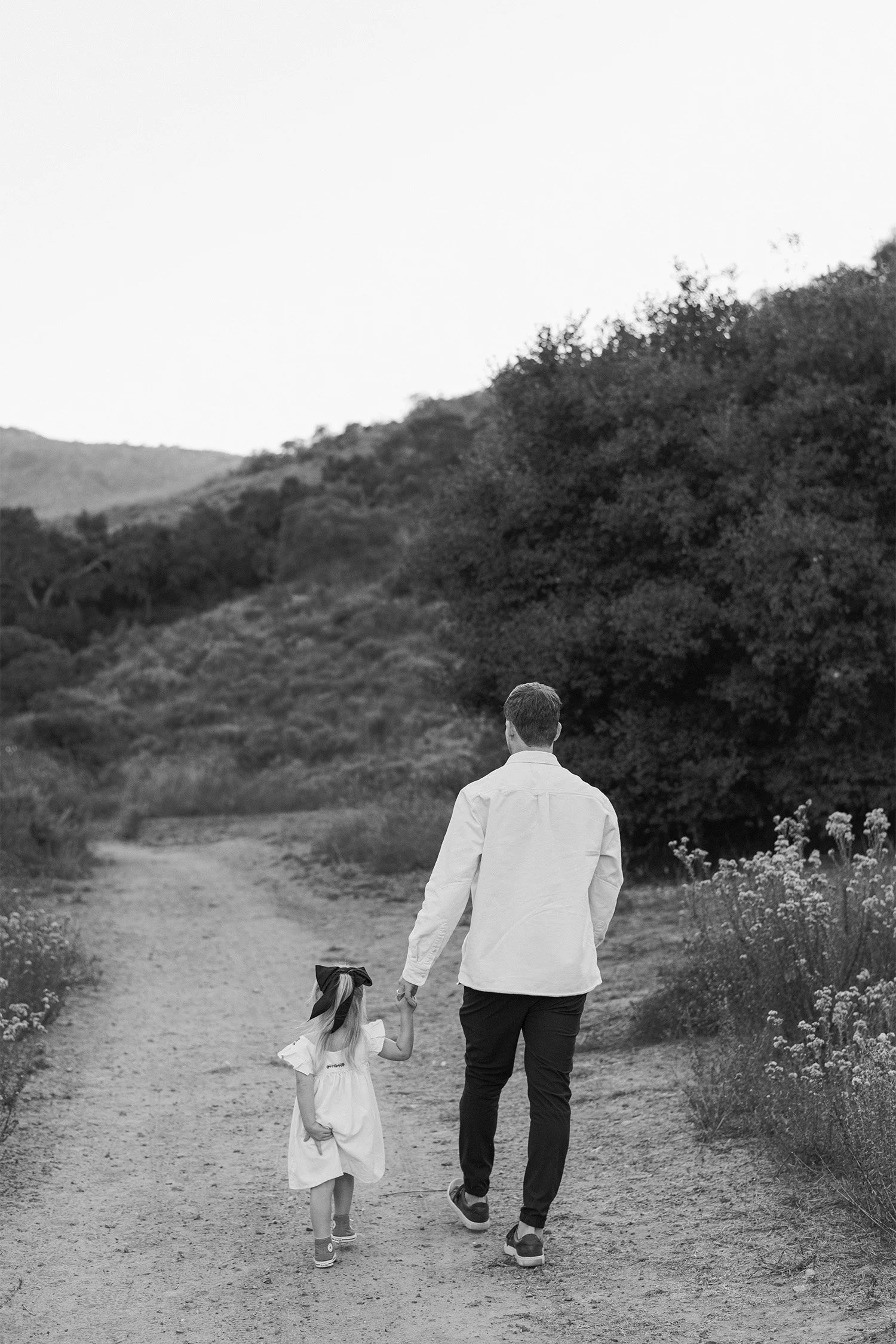 Family photography session featuring father and daughter walking hand-in-hand down a hillside trail, family photography locations in Laguna Canyon