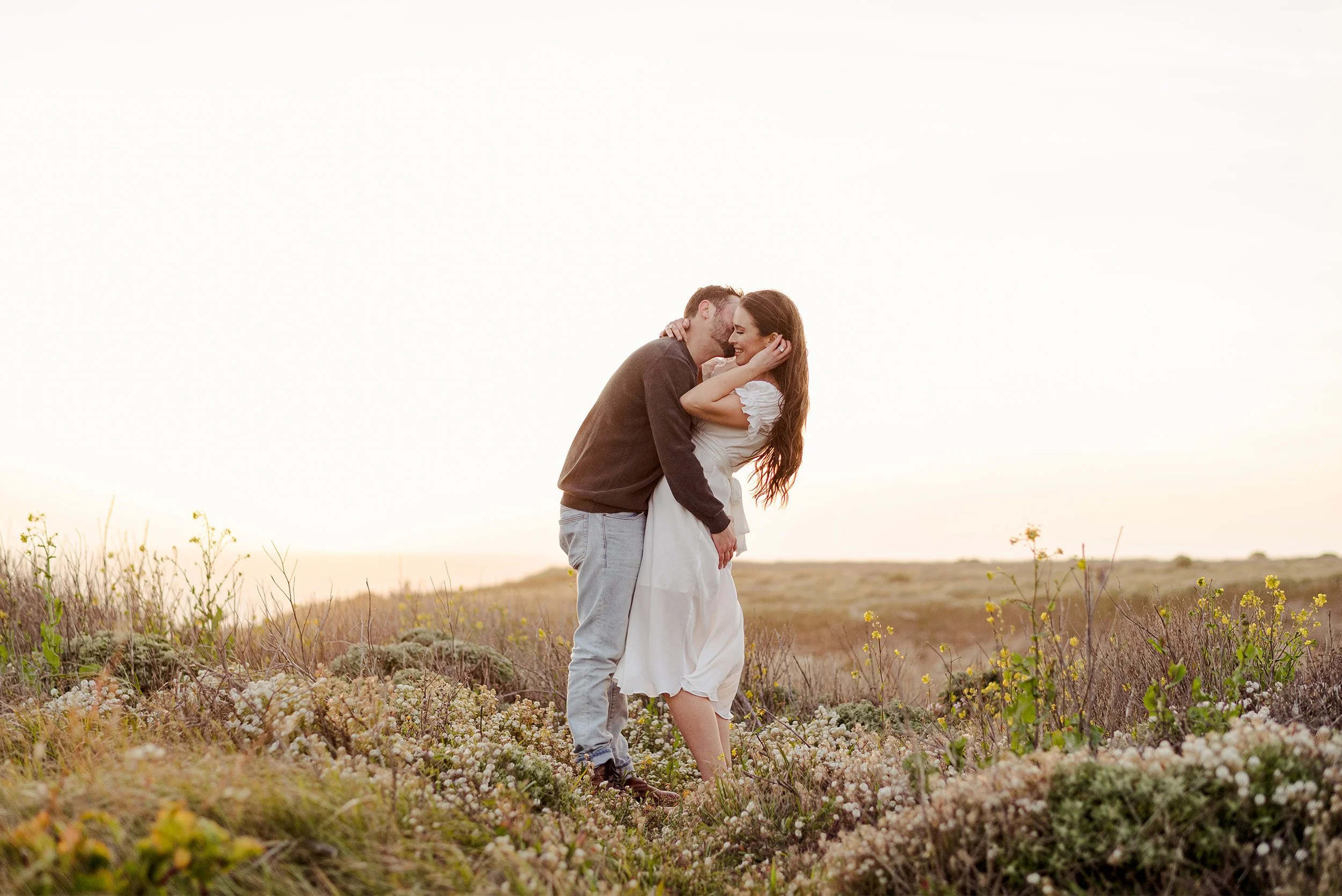 Couple embracing in coastal wildflower field at sunset, Orange County engagement photographer