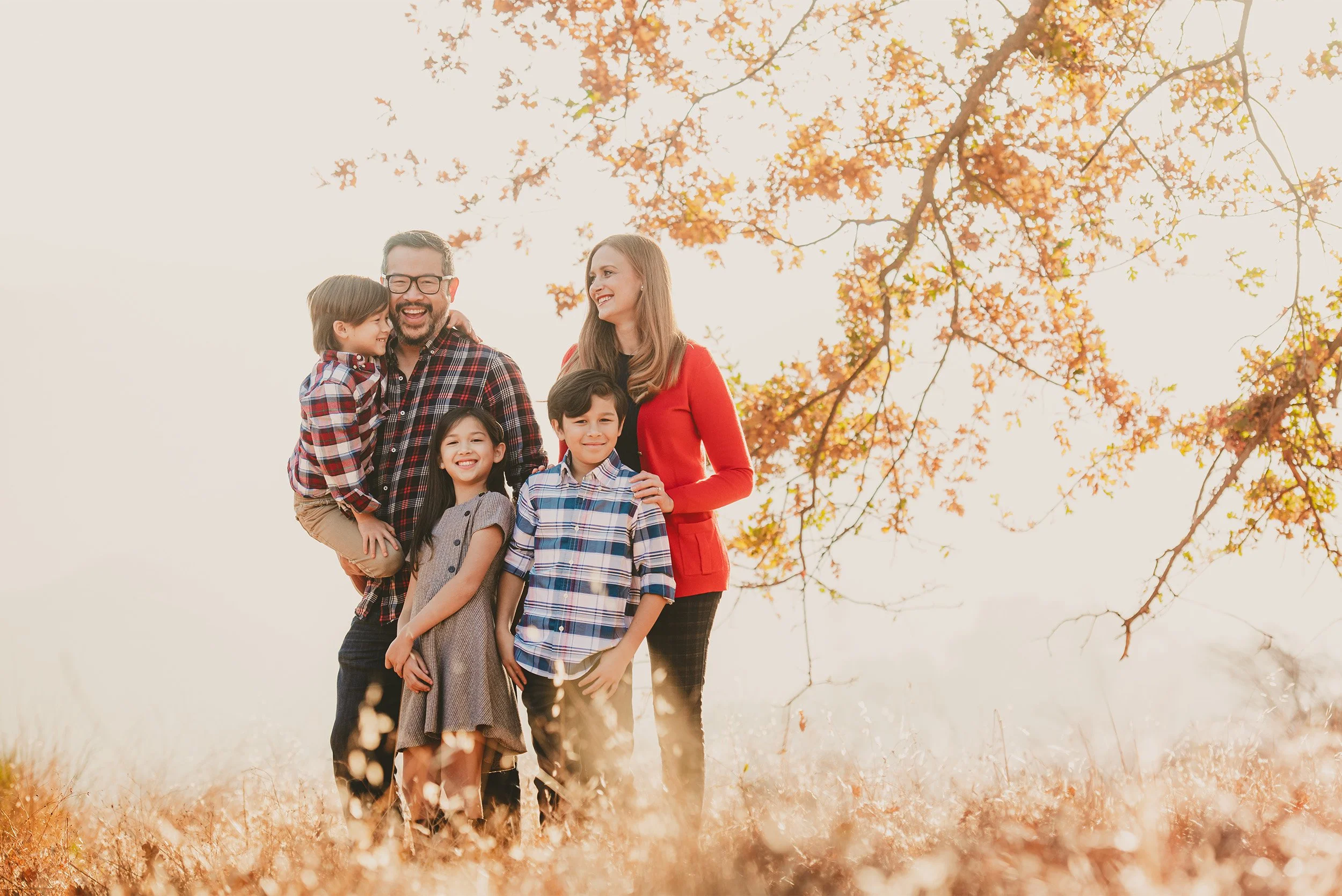 Orange County family photographer photographs family of five smiling together under golden autumn tree