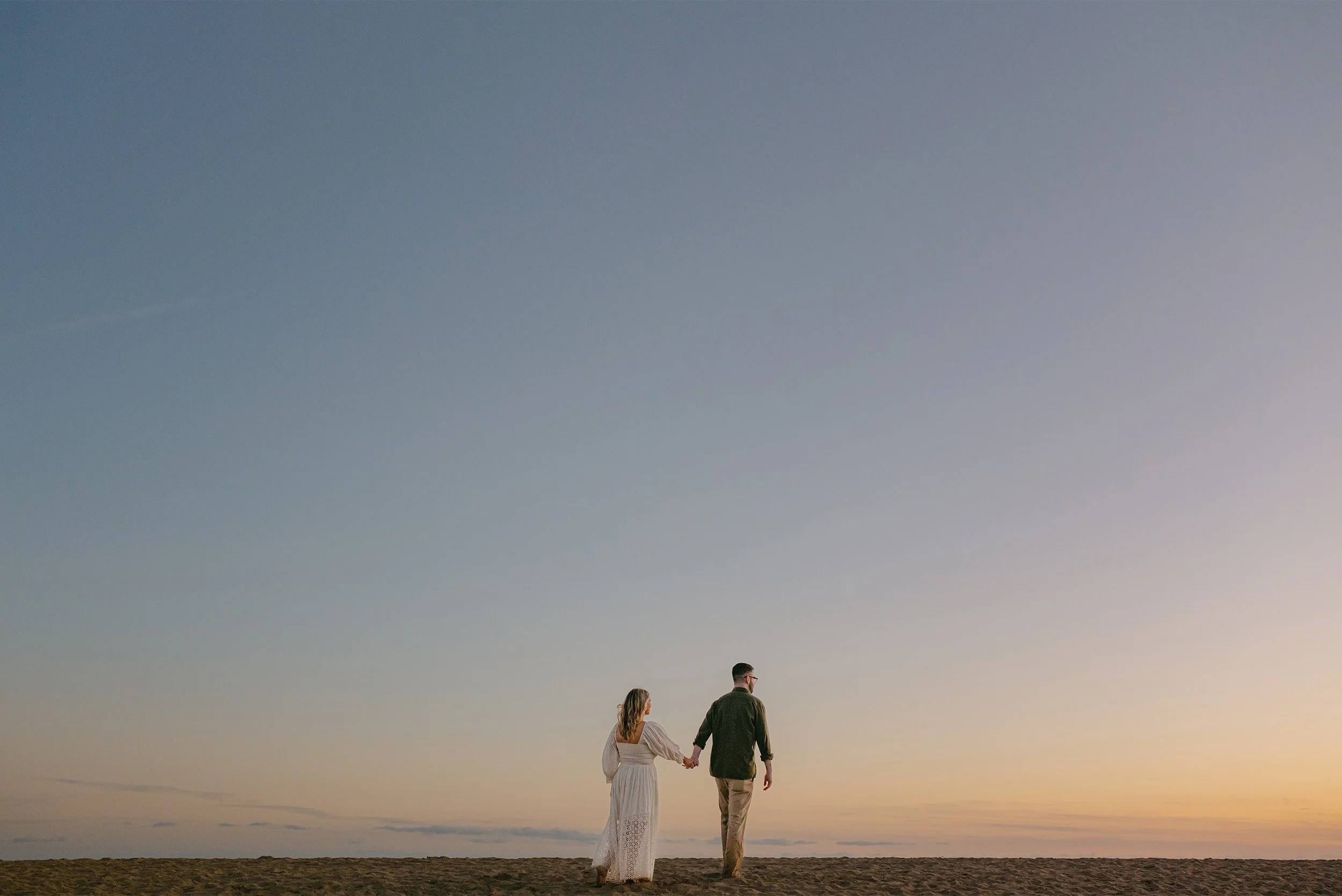 Award-winning engagement photographer in Orange County captures couple walking along Laguna Beach beneath a dusky sky