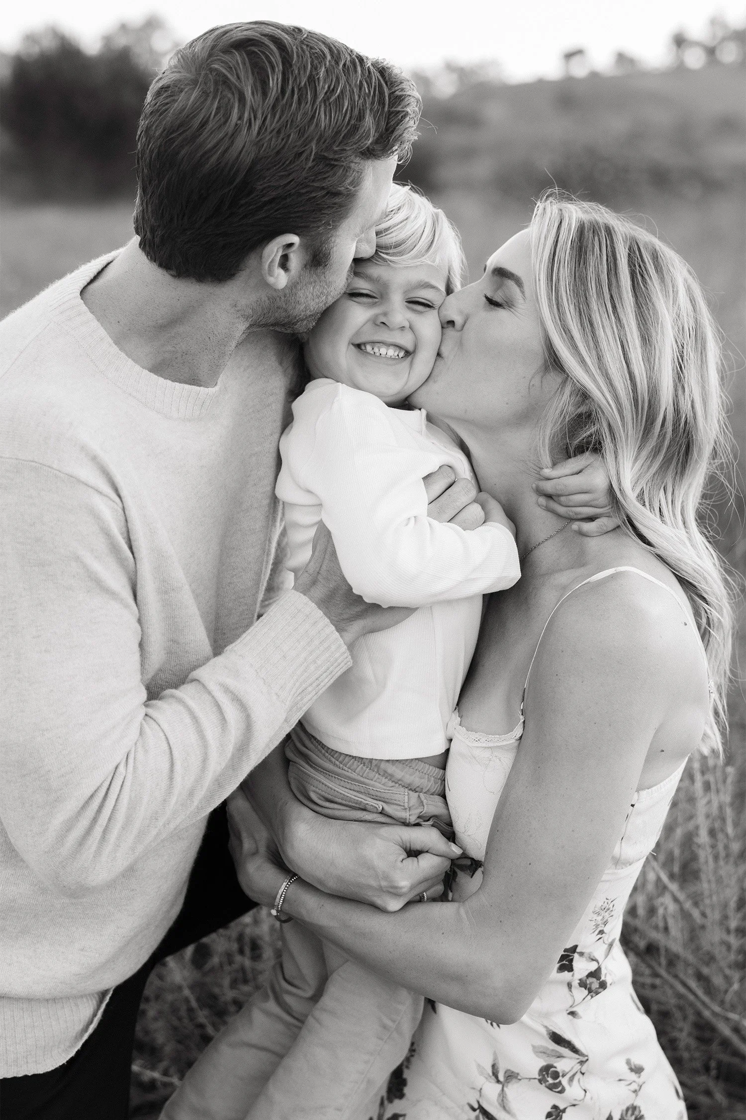 Parents kissing their giggling toddler son in a wildflower field, Black and white photo by Orange County family photographer