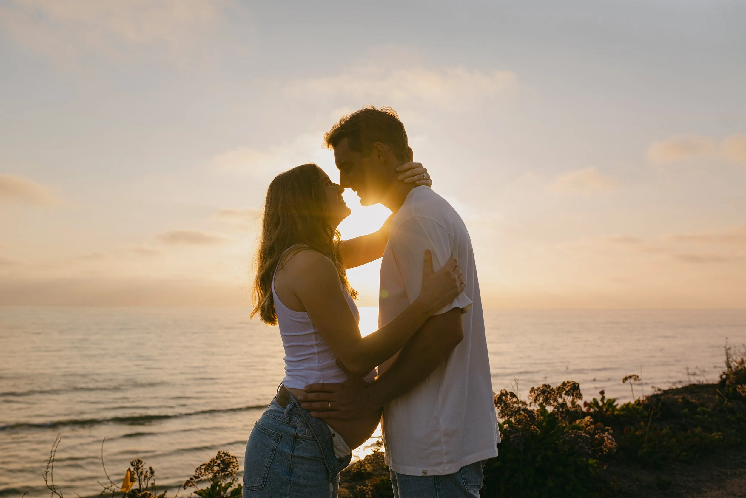 Silhouette of expecting couple embracing at sunset by the ocean, award-winning maternity photographer in Orange County