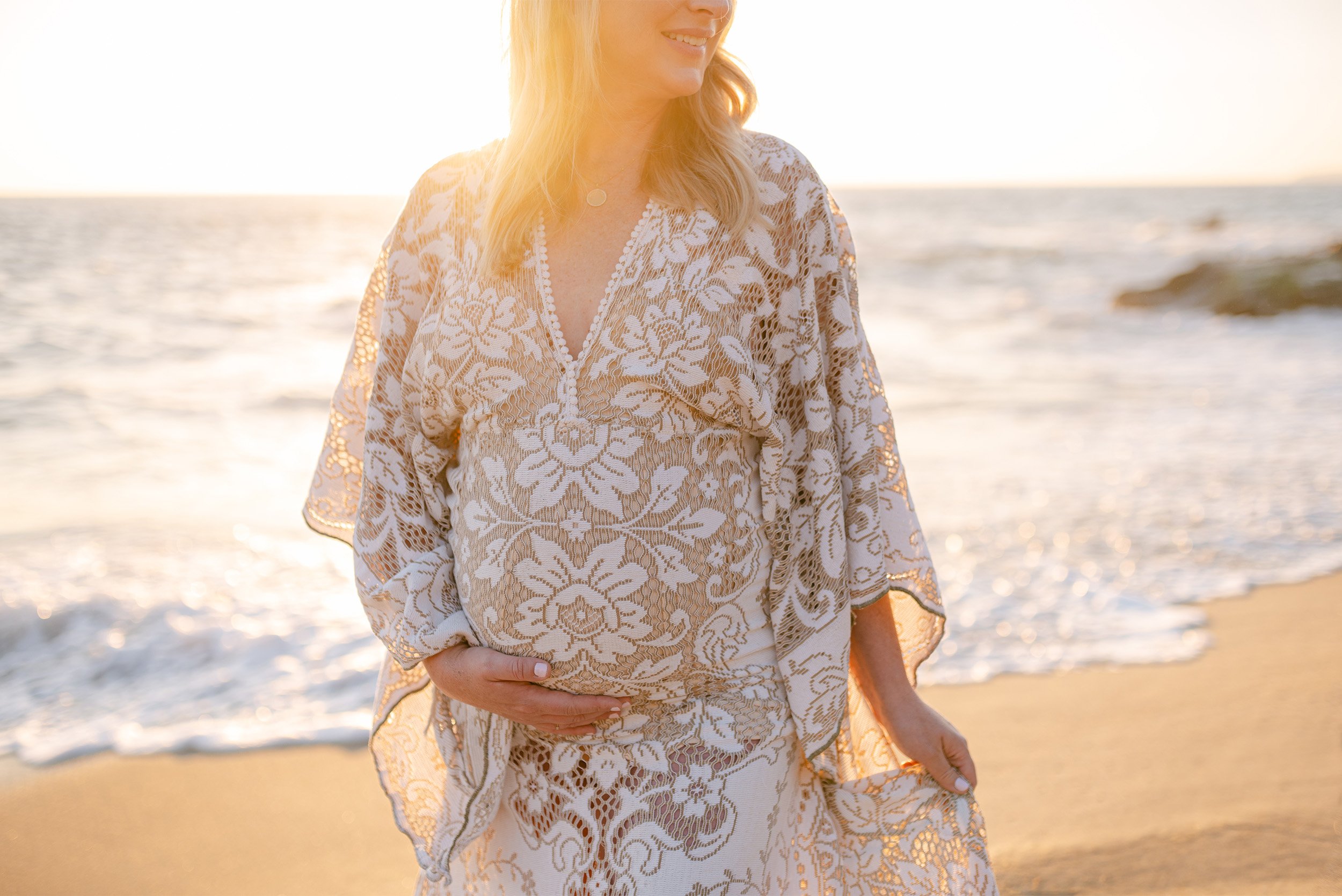 Close-up of pregnant belly in lace dress on beach at golden hour, Orange County maternity photographer