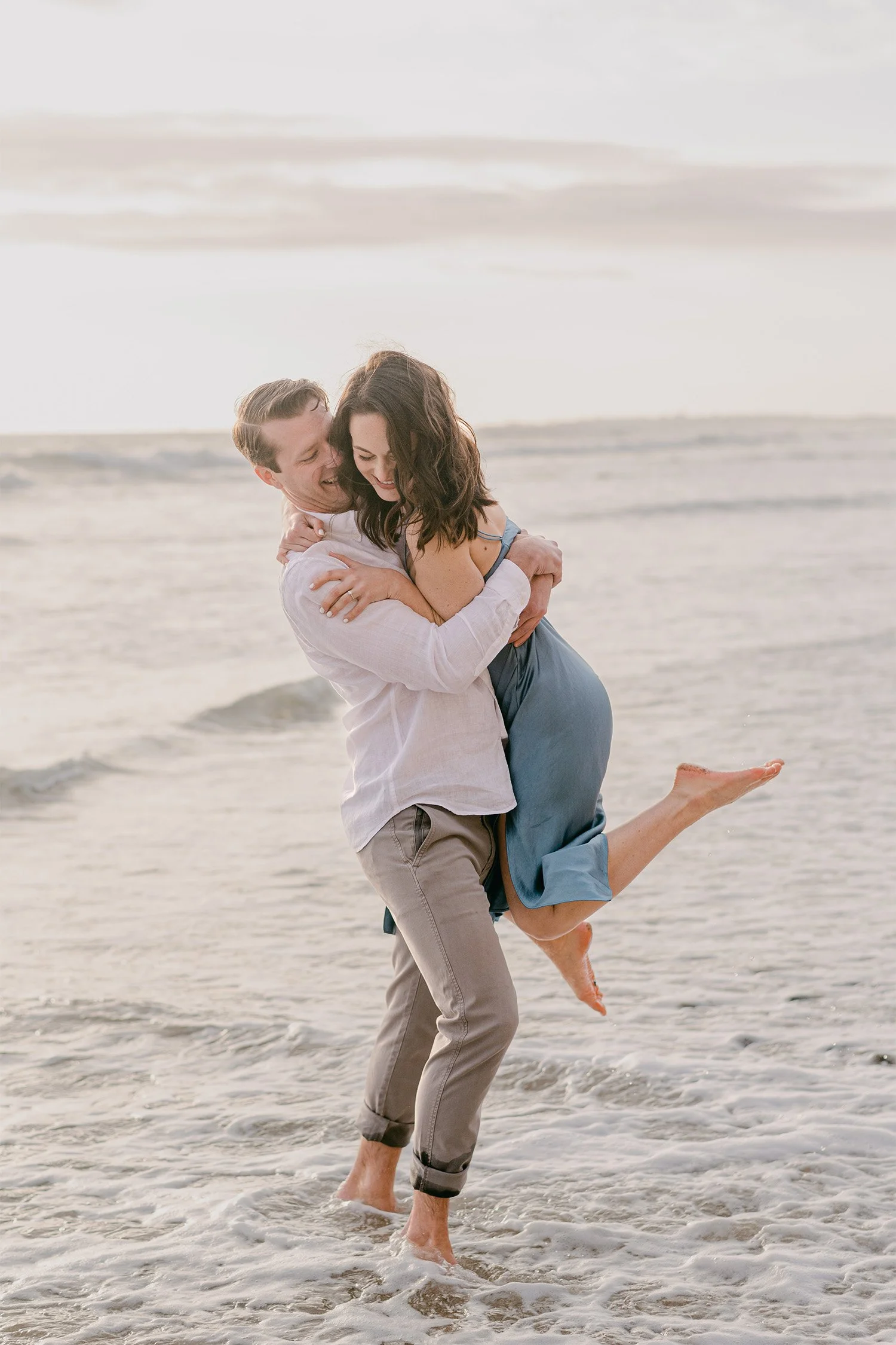 Award-winning engagement photographer in Orange County captures playful moment of man lifting fiancée on the beach