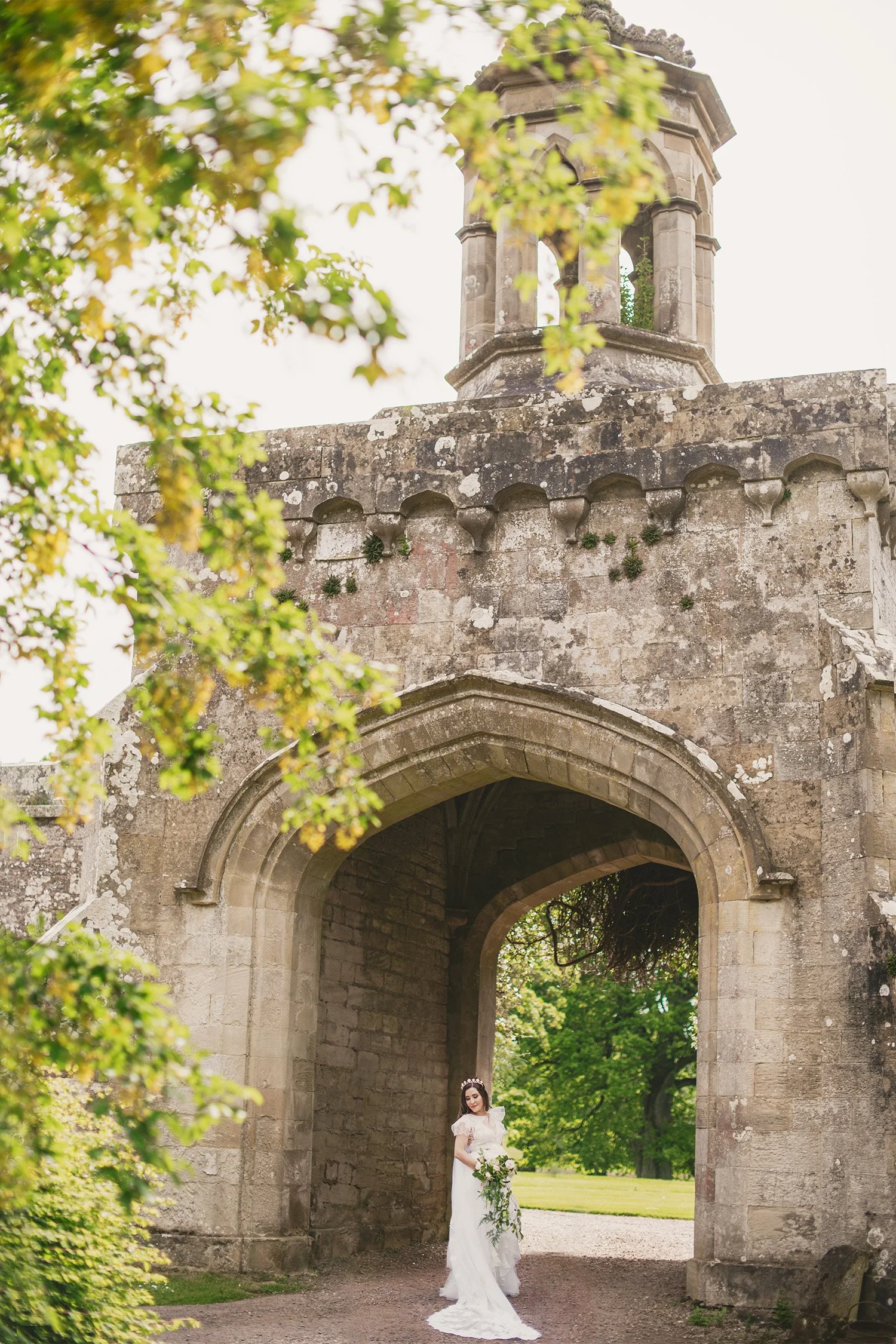 Bride standing under a stone archway at a castle wedding venue, destination wedding photography