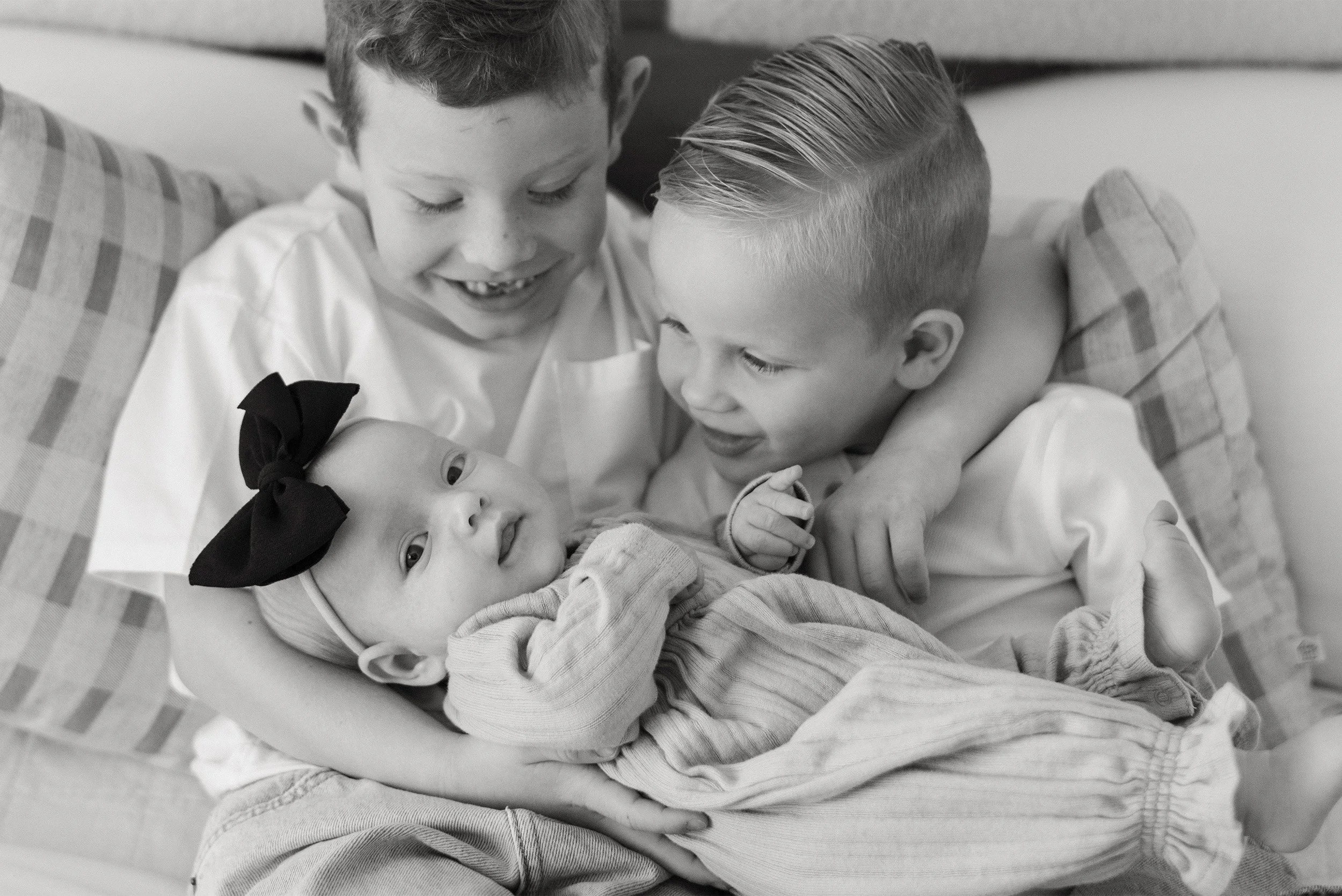 Black and white photo of two brothers smiling at baby sister, award-winning baby photographer Orange County