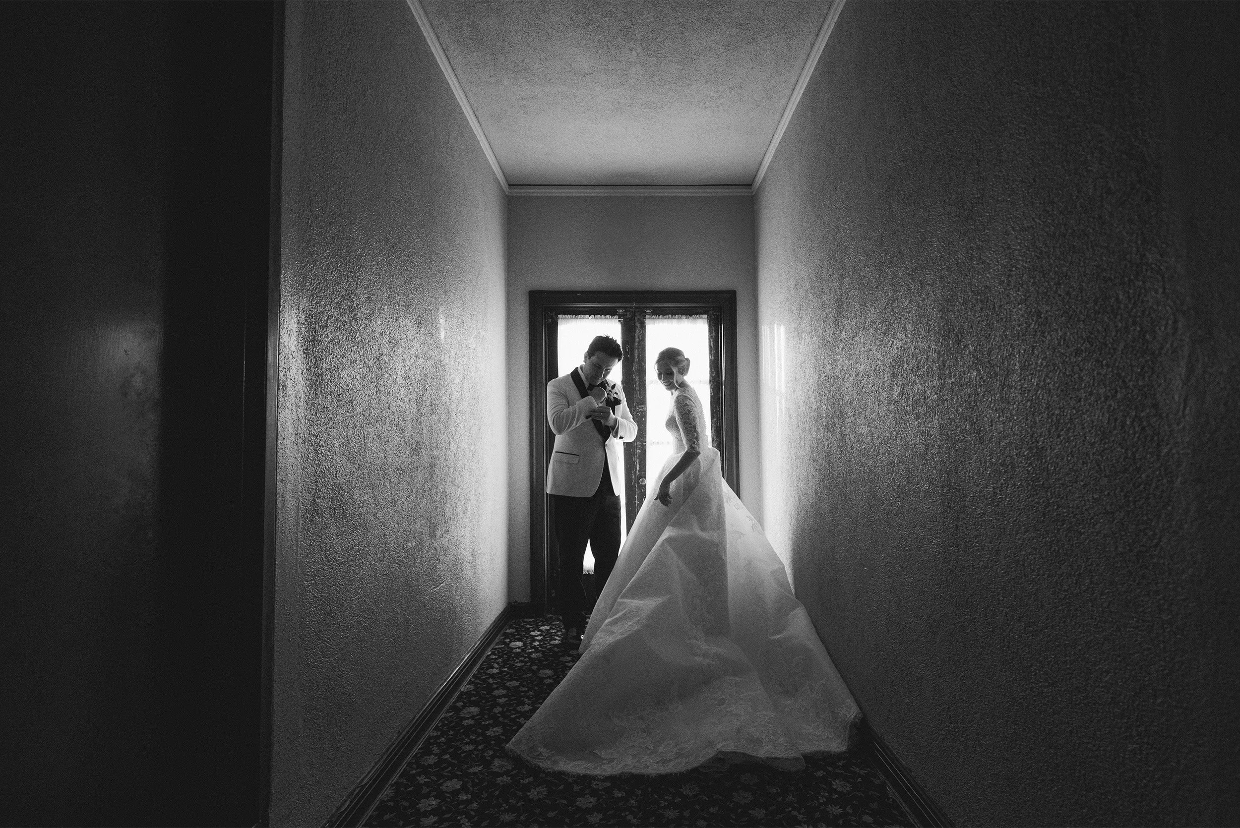 Orange County wedding photographer captures bride and groom silhouetted in vintage hallway at The Ebell of Los Angeles with lace wedding gown train, black and white