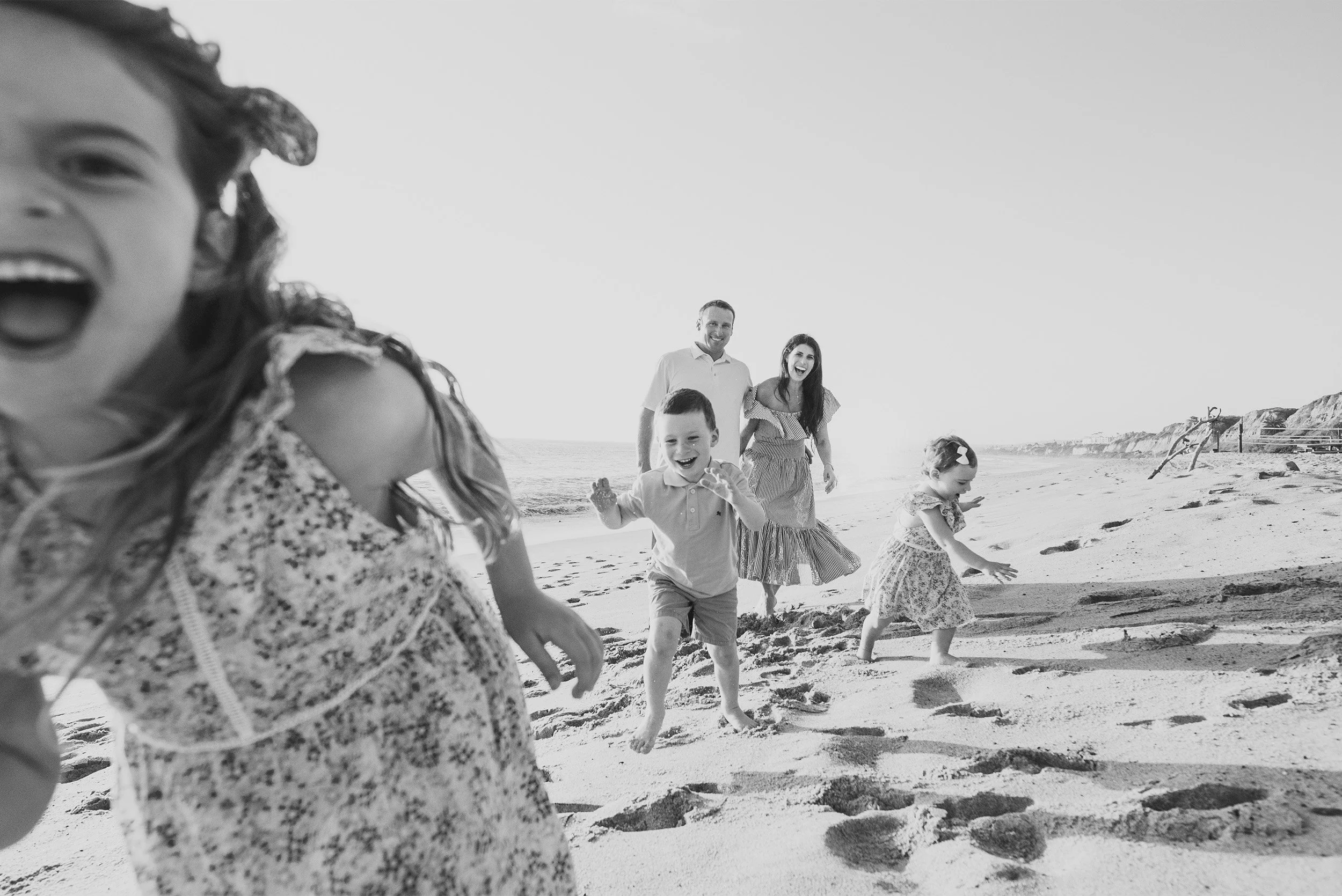 Orange County family photographer captures candid black and white image of children running and laughing on the beach