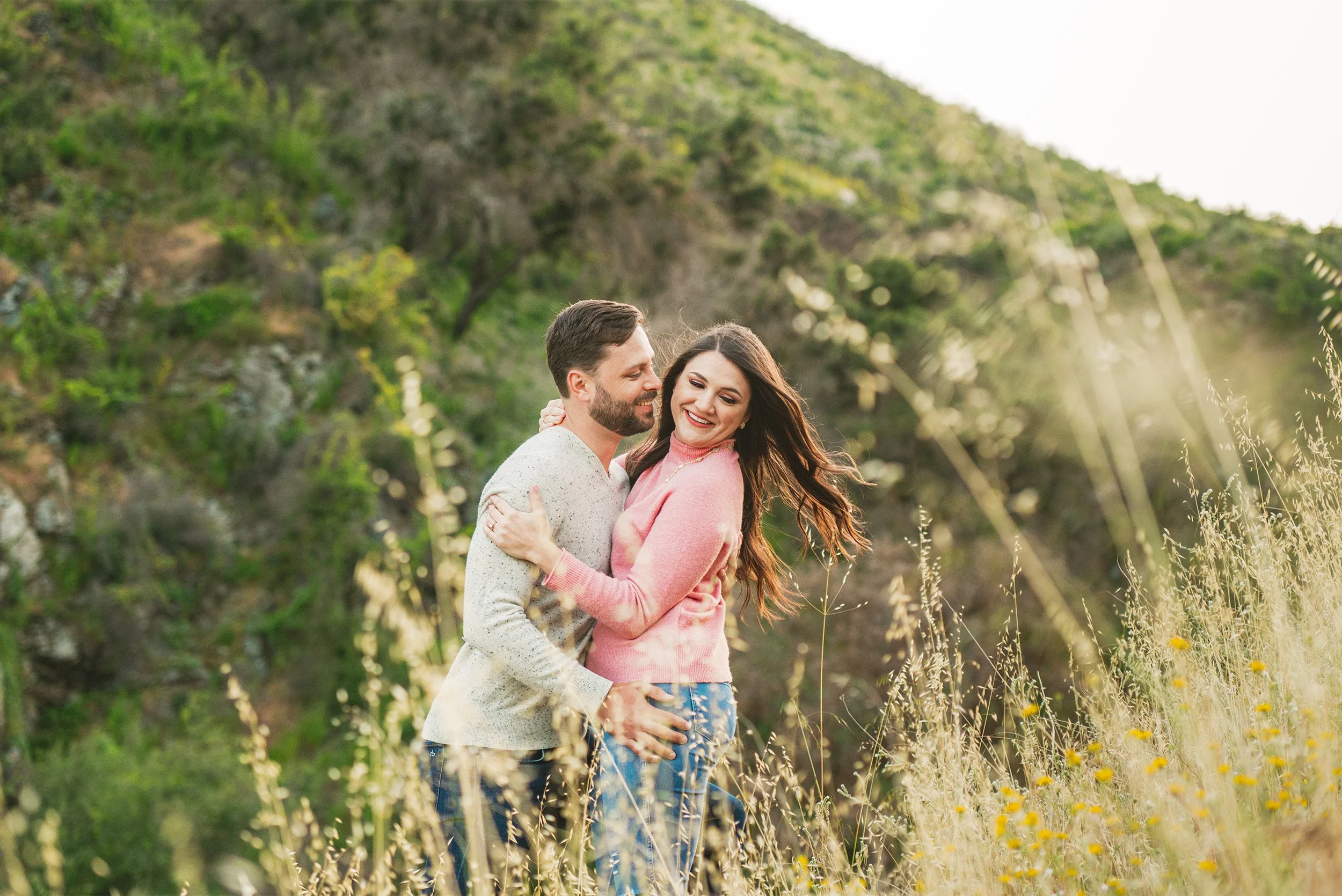 Couple embracing on hillside with windswept hair, highly recommended engagement photographer Orange County
