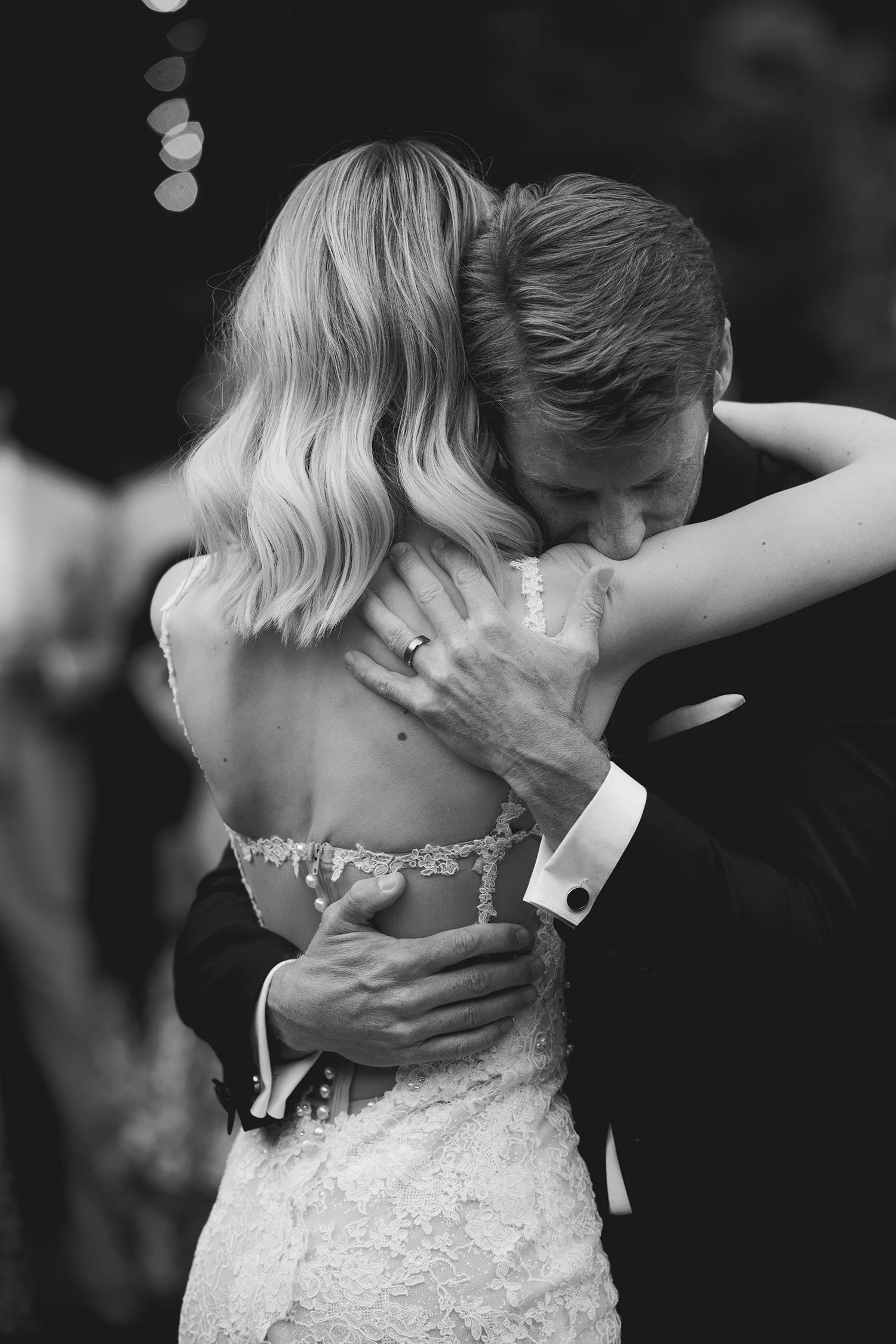 Award-winning wedding photographer in Orange County captures intimate embrace showing intricate lace back detail of wedding gown, black and white, Gardener Ranch wedding venue in Carmel Valley