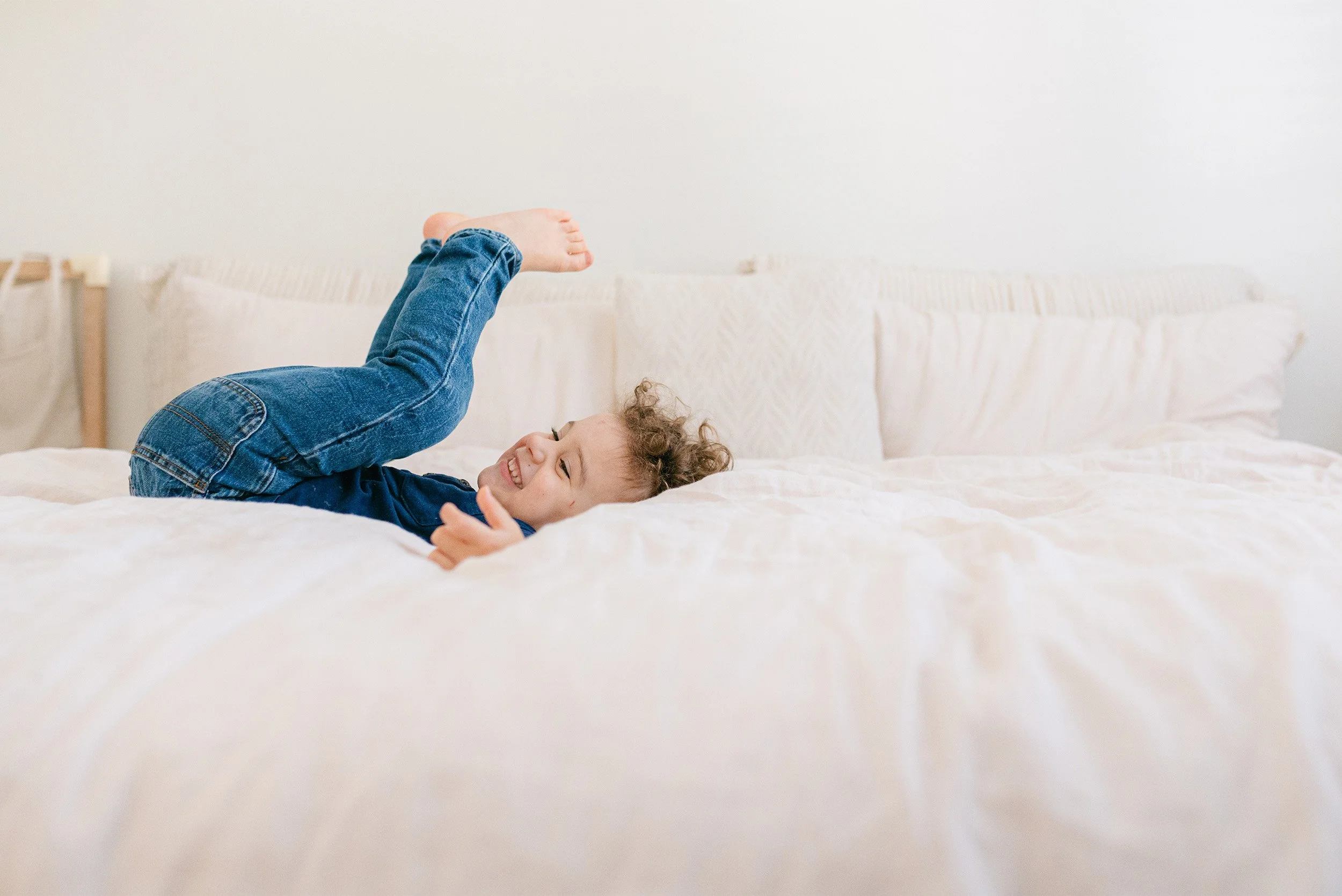 Lifestyle family photography featuring boy playing joyfully on bed at home, Orange County family photographer