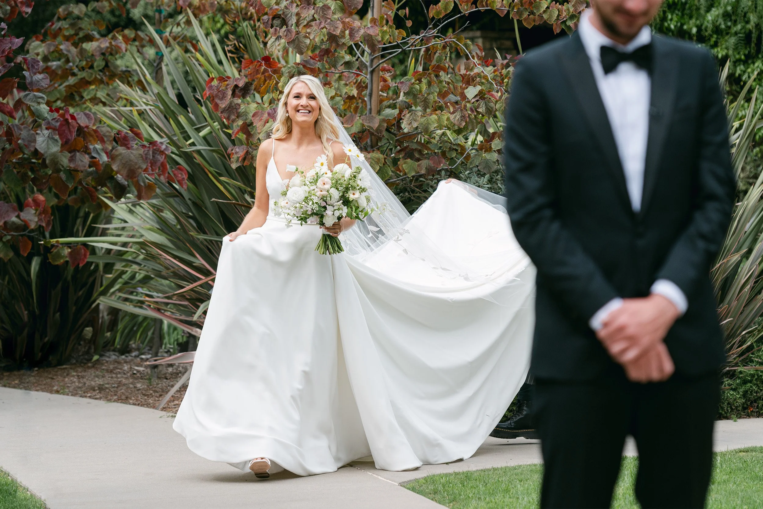 Highly recommended wedding photographer in Orange County captures bride joyfully walking toward groom with white floral bouquet during first look at The Ranch at Laguna Beach