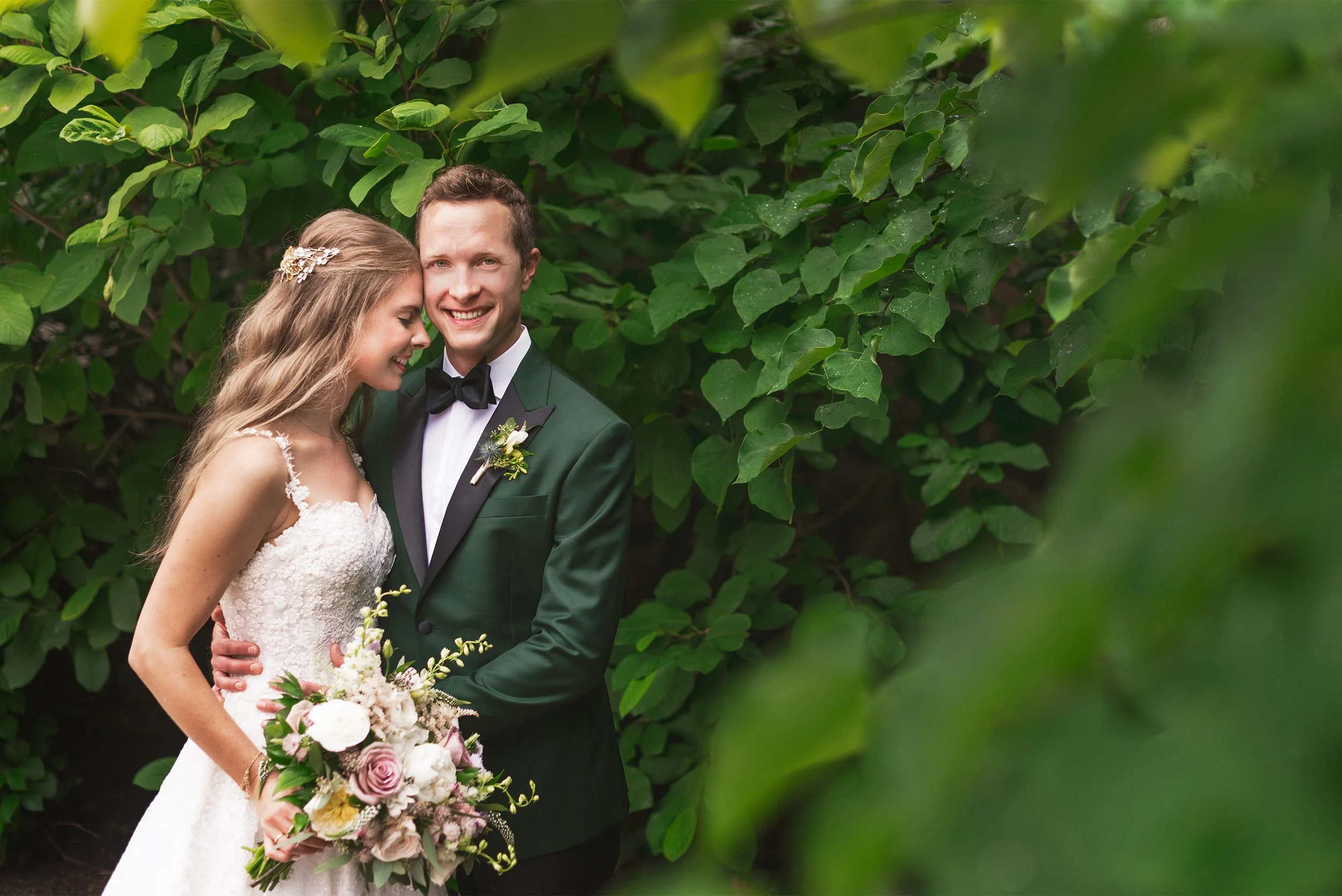 Bride and groom smiling together in green foliage garden, green tuxedo wedding portrait