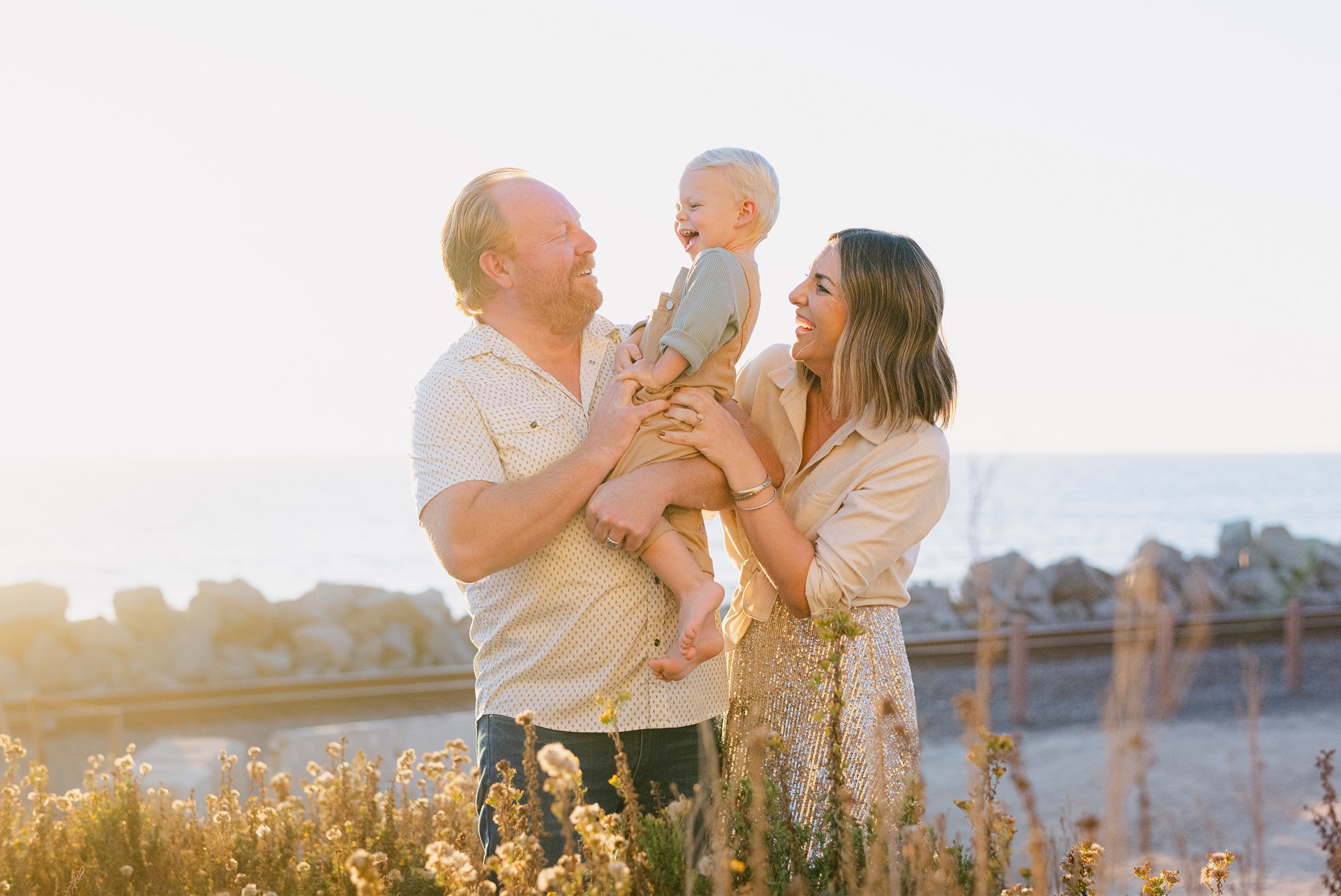 Orange County family portrait photography featuring parents laughing with son near the ocean at sunset