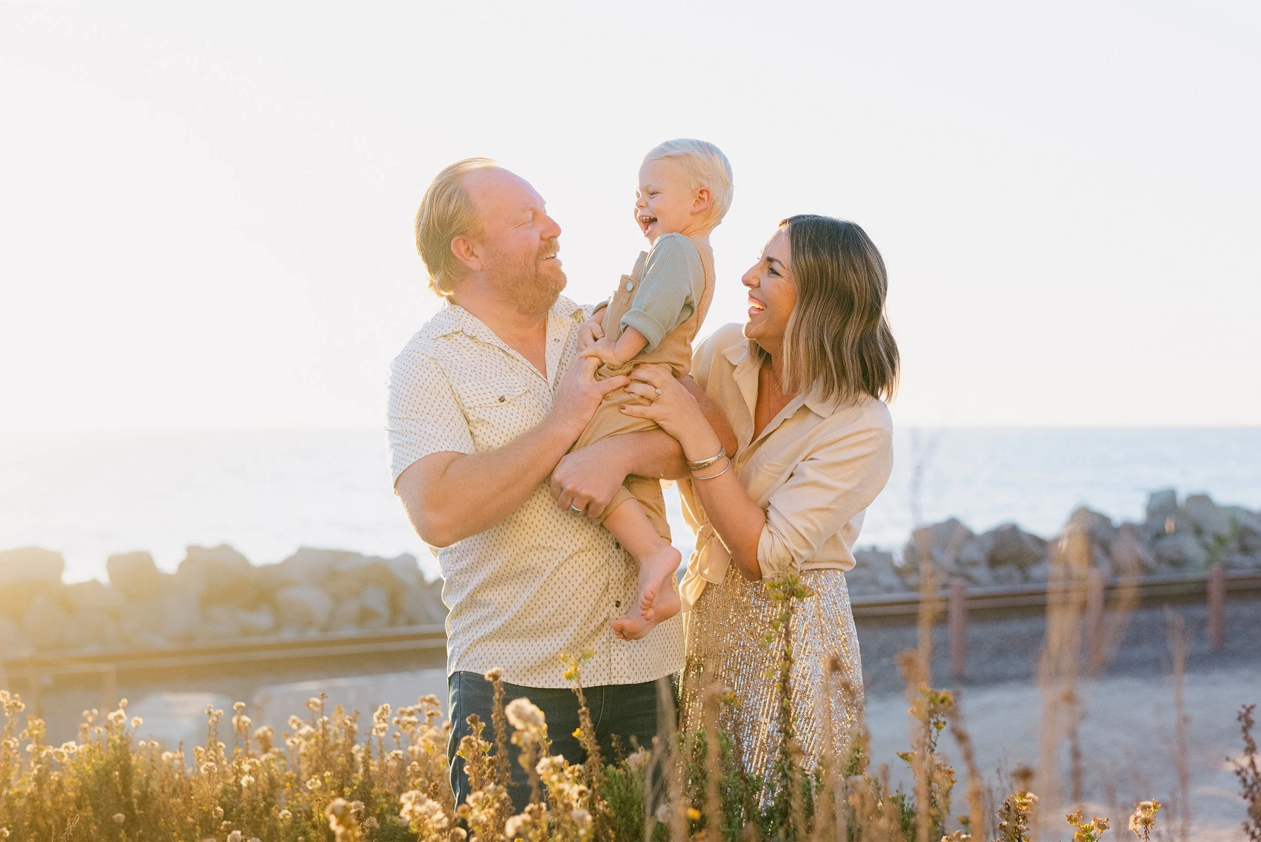 Orange County family portrait photography featuring parents laughing with son at San Clemente Beach at sunset