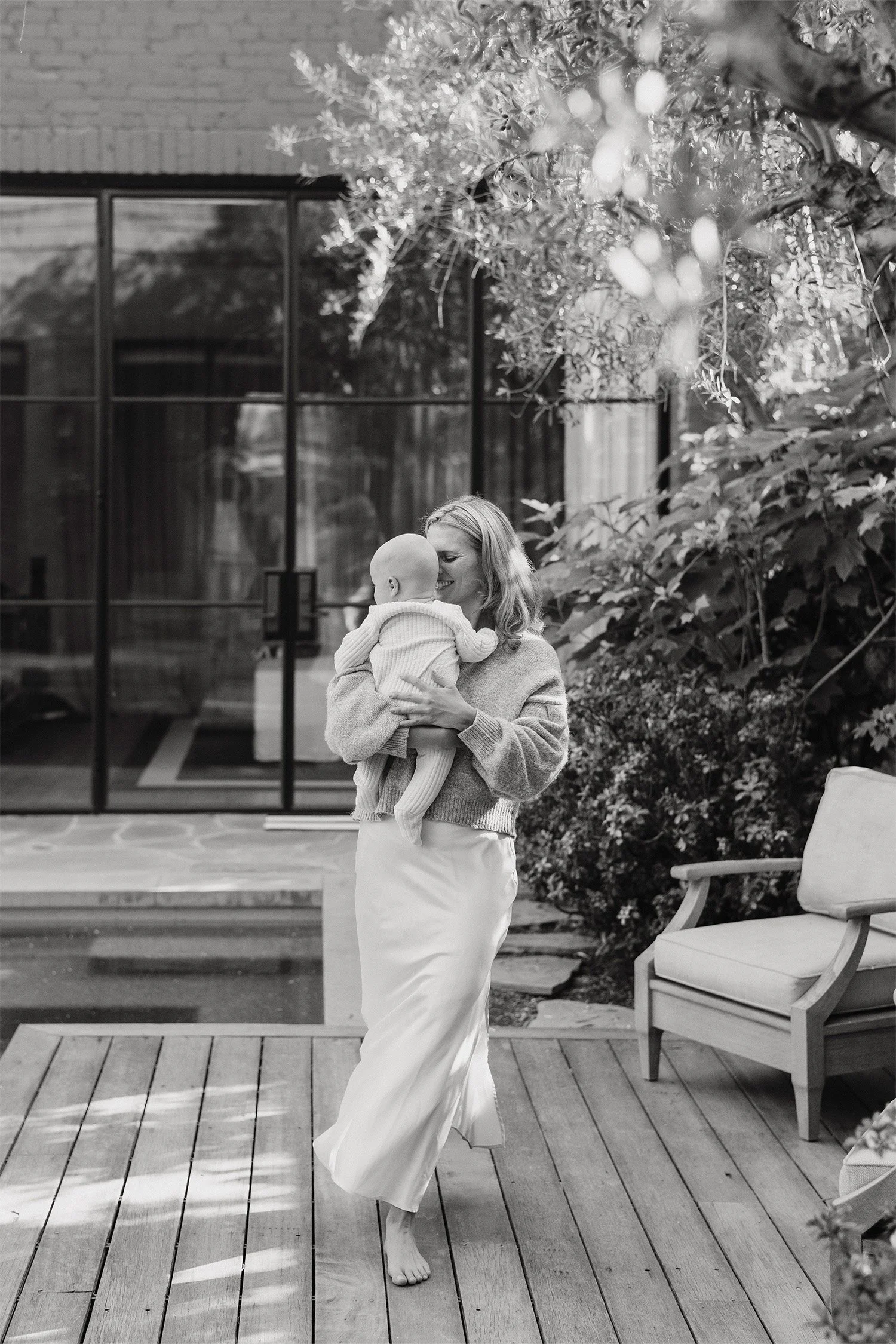 Mother carrying baby across a modern backyard patio, Highly recommended family photographer in Orange County