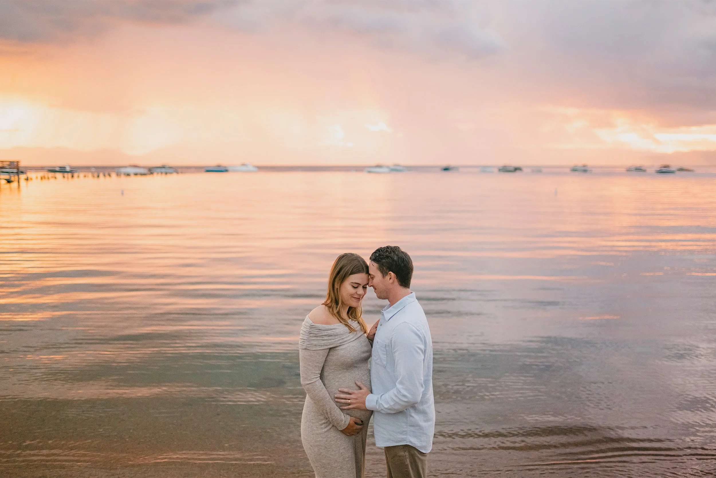 Pregnant couple embracing forehead to forehead at sunset on the water, highly recommended maternity photographer Orange County