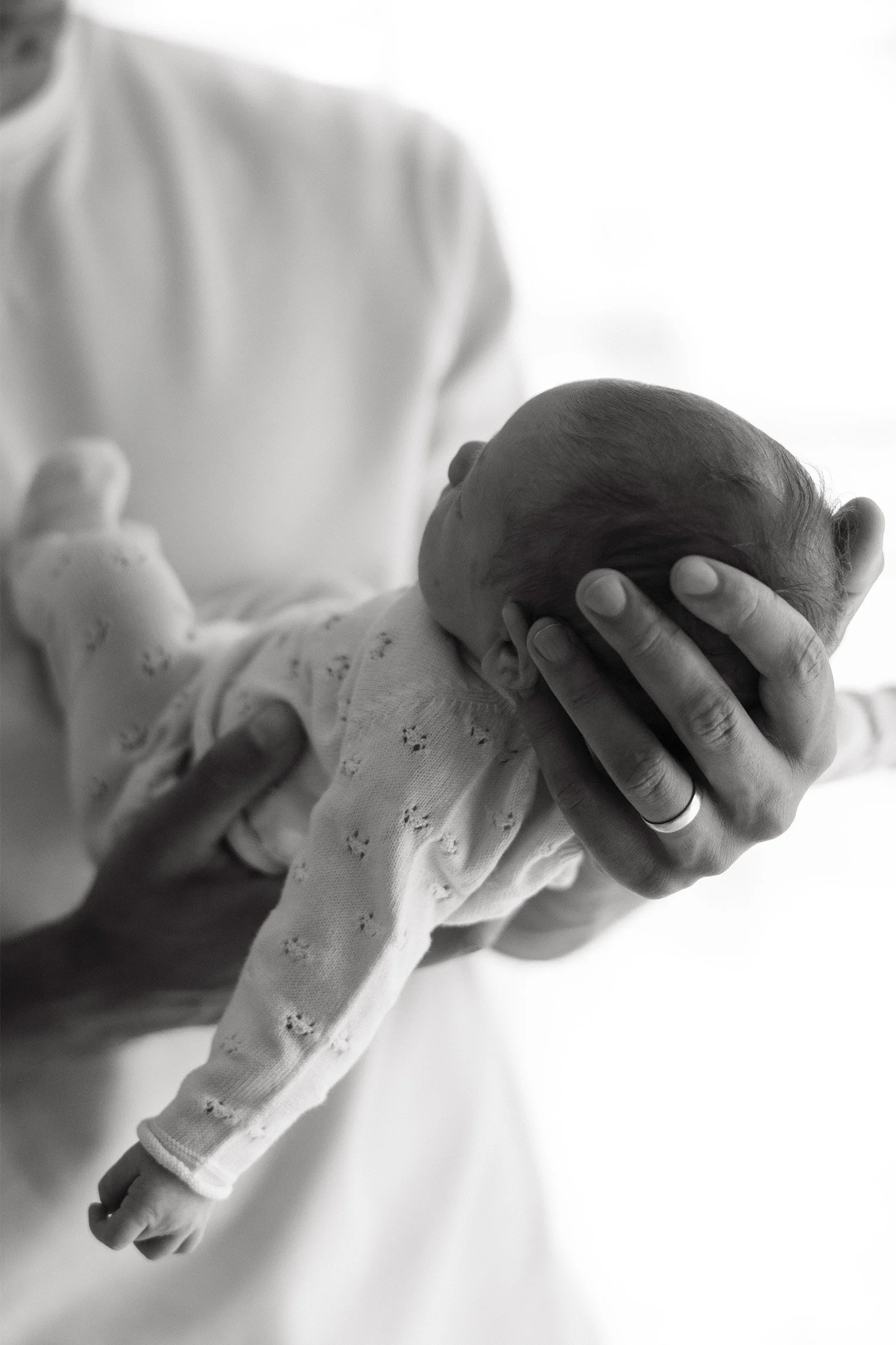 Black and white close-up of father's hand cradling newborn's head, highly recommended baby photographer