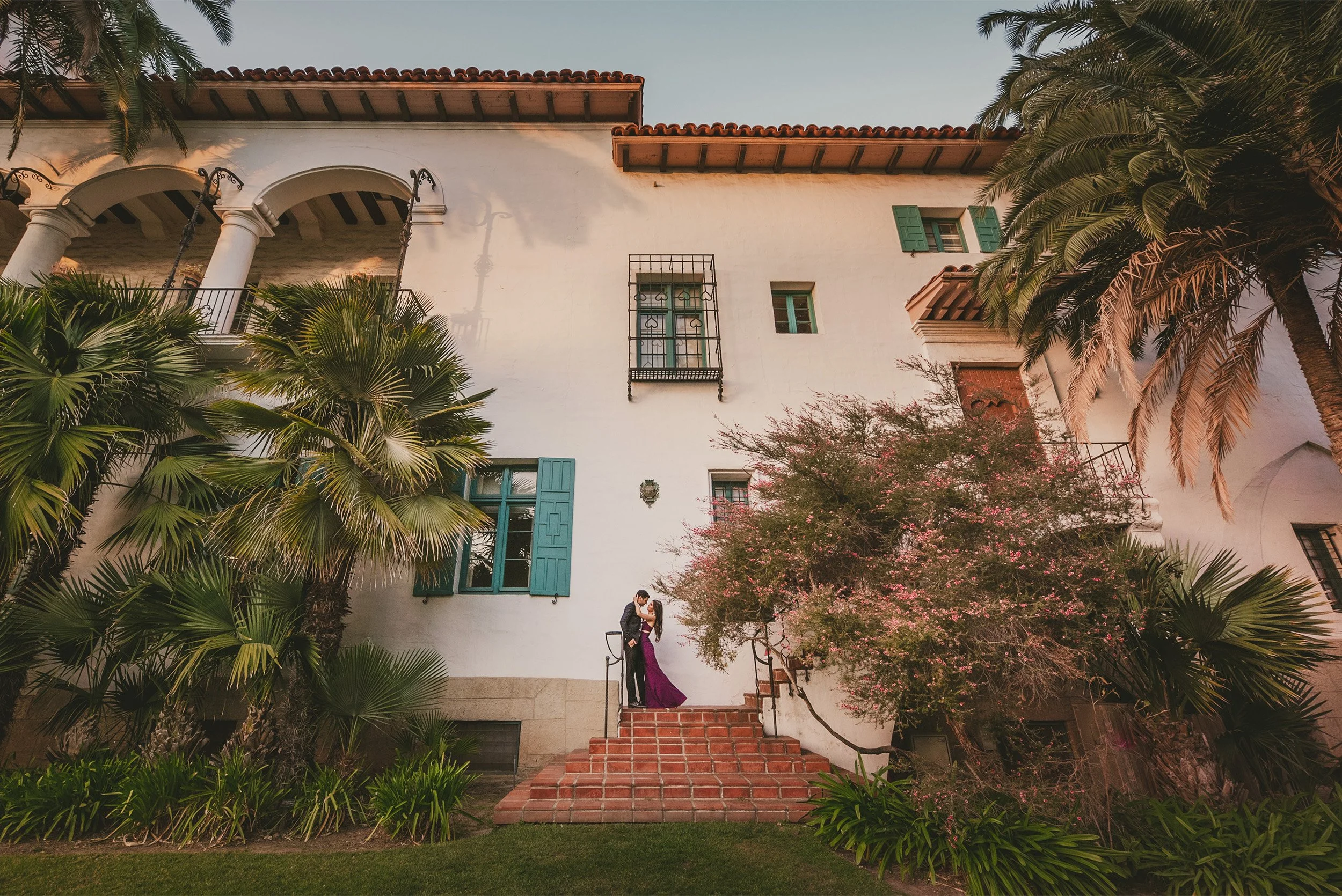 Couple kissing on the steps of a Spanish colonial mansion surrounded by palm trees, Santa Barbara Courthouse engagement photos
